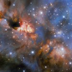 A nebula with stars. The center of the image from top-left to bottom-right glows brightly with the light of newly forming stars and is partially obscured by dark dust. Colored layers of gas and dust billow out across the rest of the image. Foreground stars with large diffraction spikes speckle the nebula.