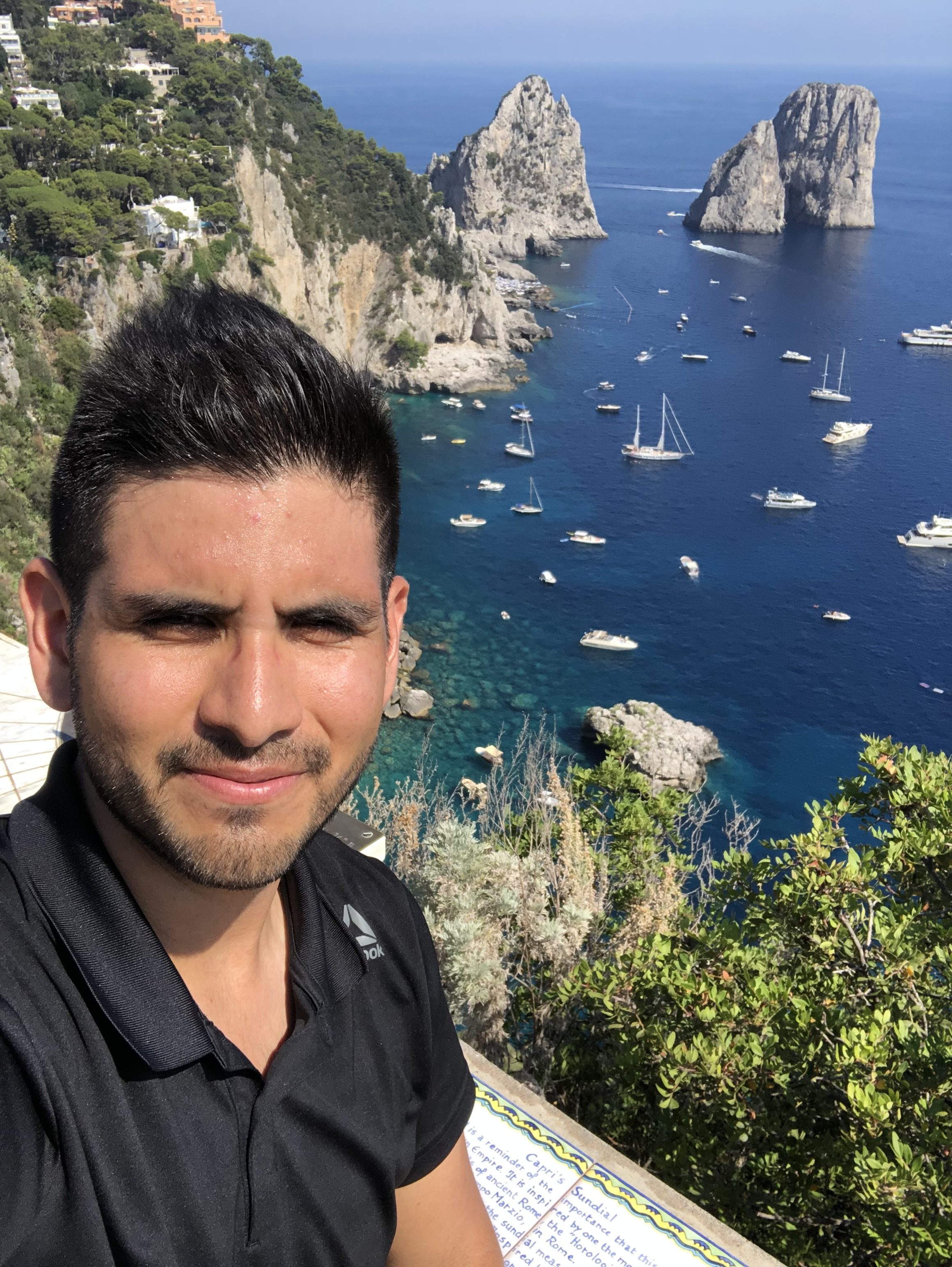Juan Pablo Leon is standing on a cliff over a harbor filled with boats.