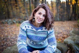 Portrait photo of a smiling woman sitting in a wooded outdoor area.