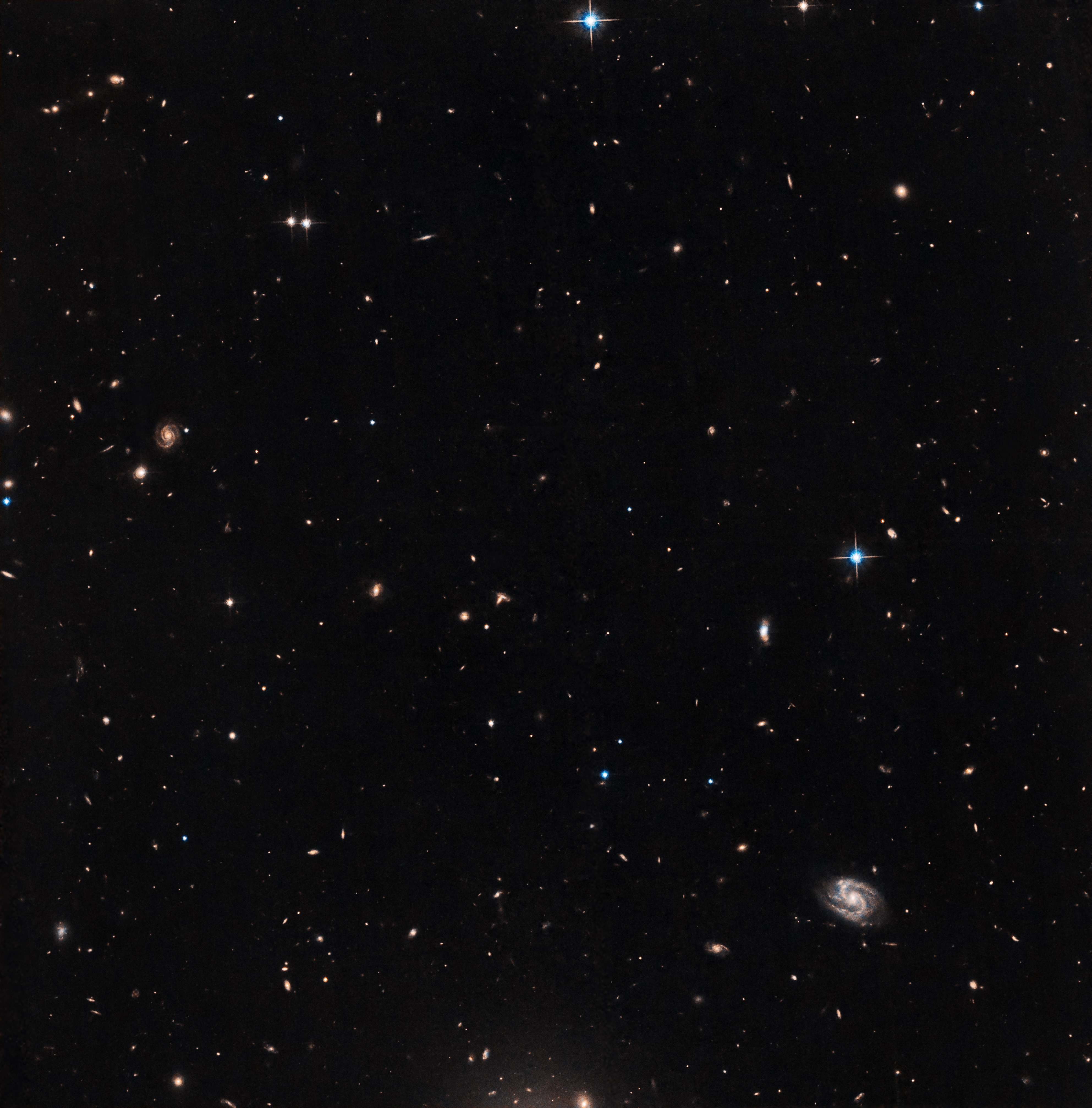 Background galaxies and stars are sprinkled across a black background. Some of the distant galaxies are spirals.