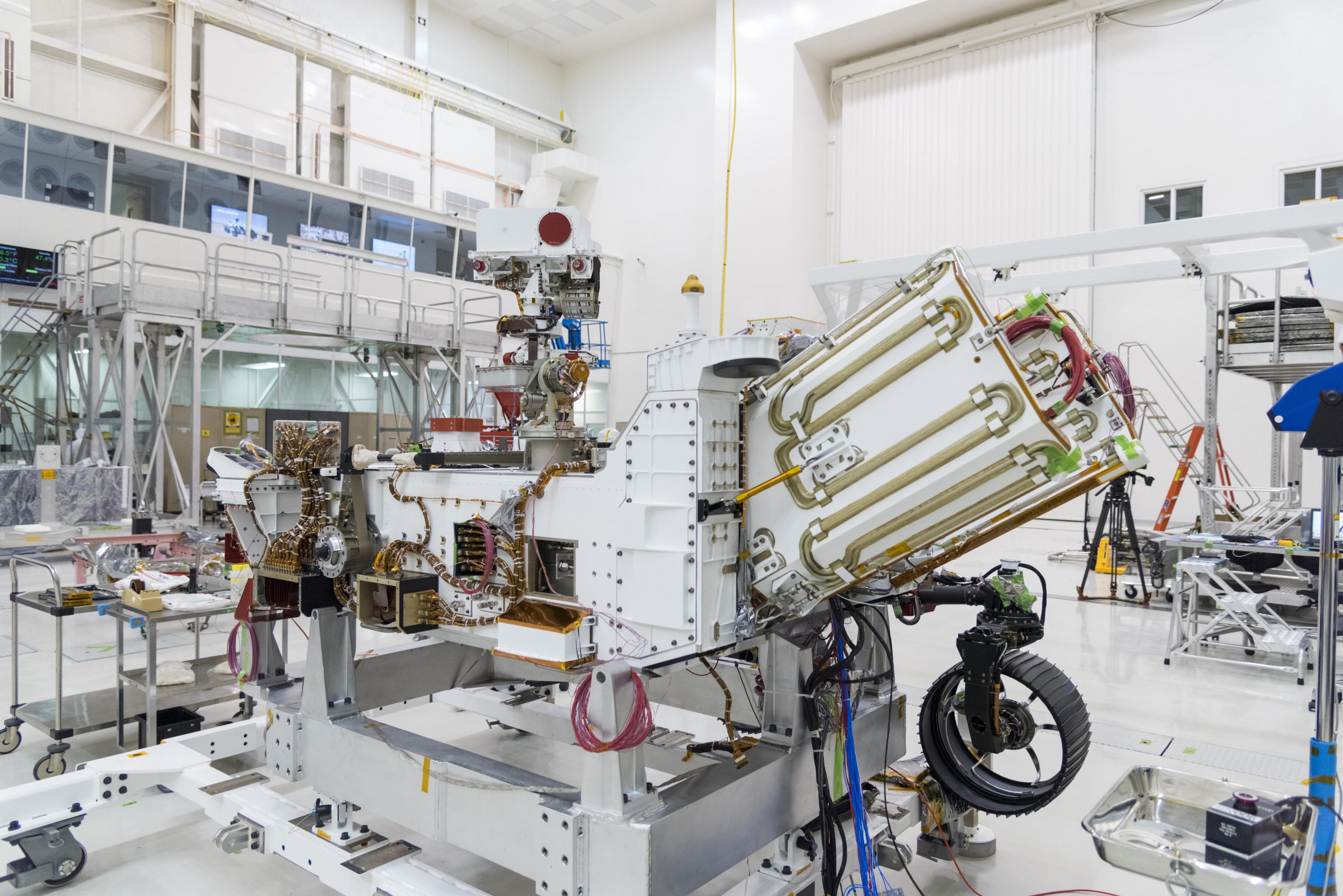 A partially assembled Mars rover in the cleanroom at JPL. The rover's Radioisotope Thermoelectric Generator is jutting from the back of the rover.