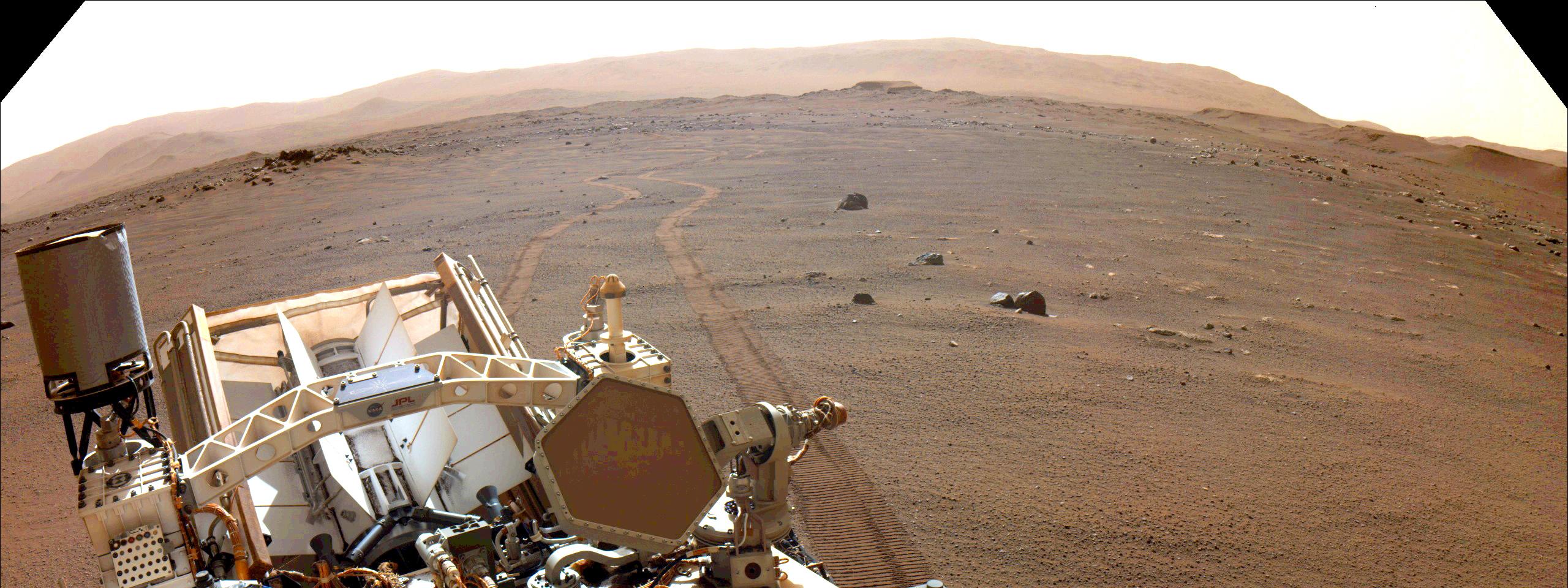 Twin wheel tracks extend to the horizon in this view over the back of the rover.