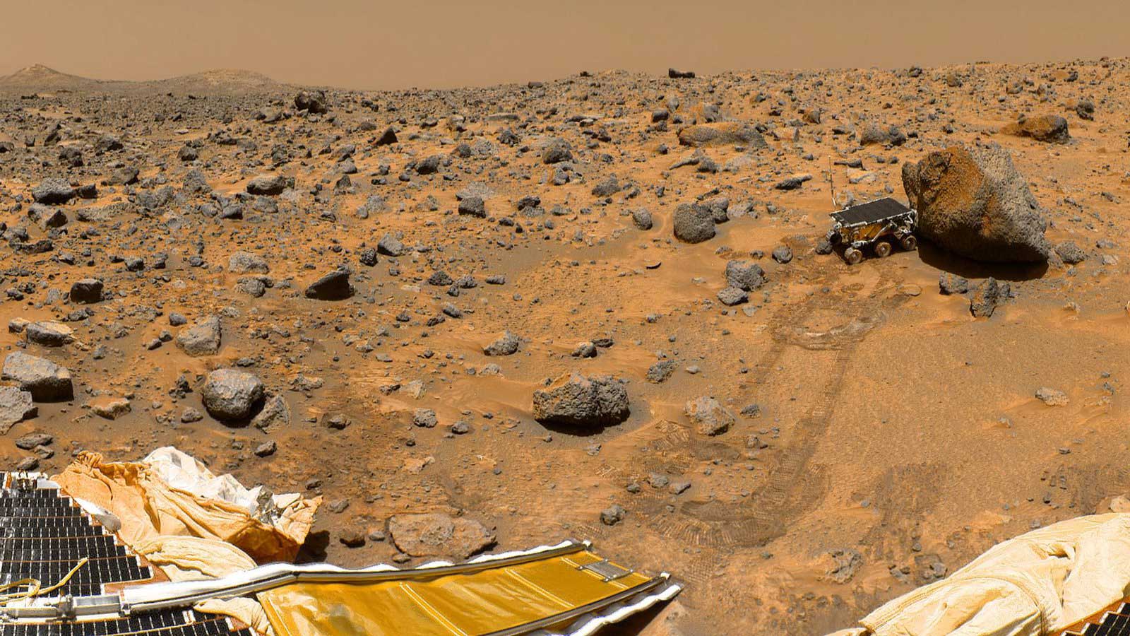 A microwave-sized rover pushes up against a rock in this landscape on Mars. The rover's landing platform and tire tracks in the soil also are visible.