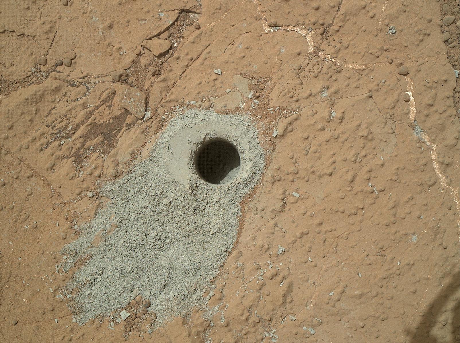 A drilled hole surrounded by gray dust on the red surface of Mars.