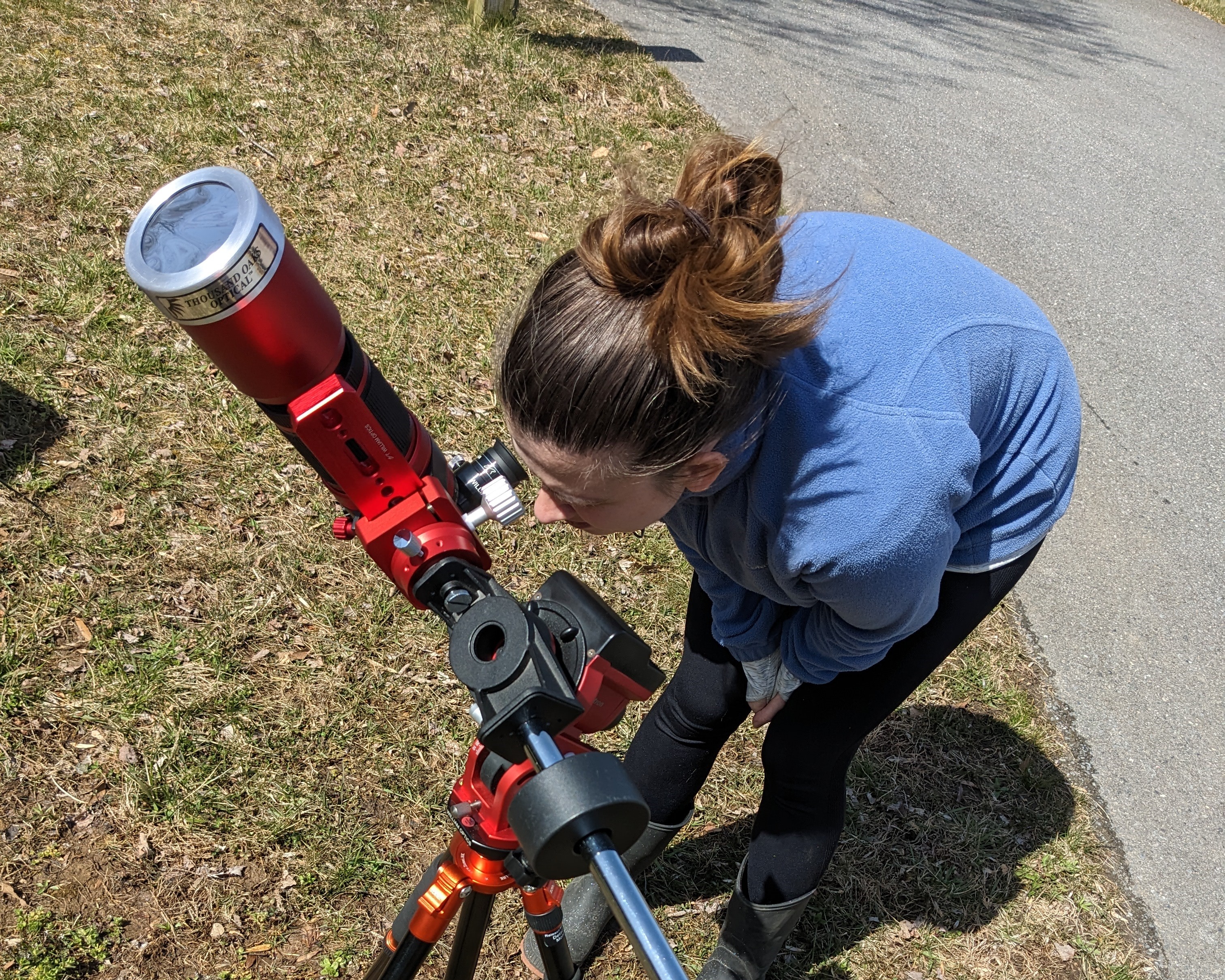 A woman in blue looking at the Sun through a red telescope with a solar filter.