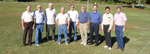 Photo of 9 men standing in a field and posing for the camera