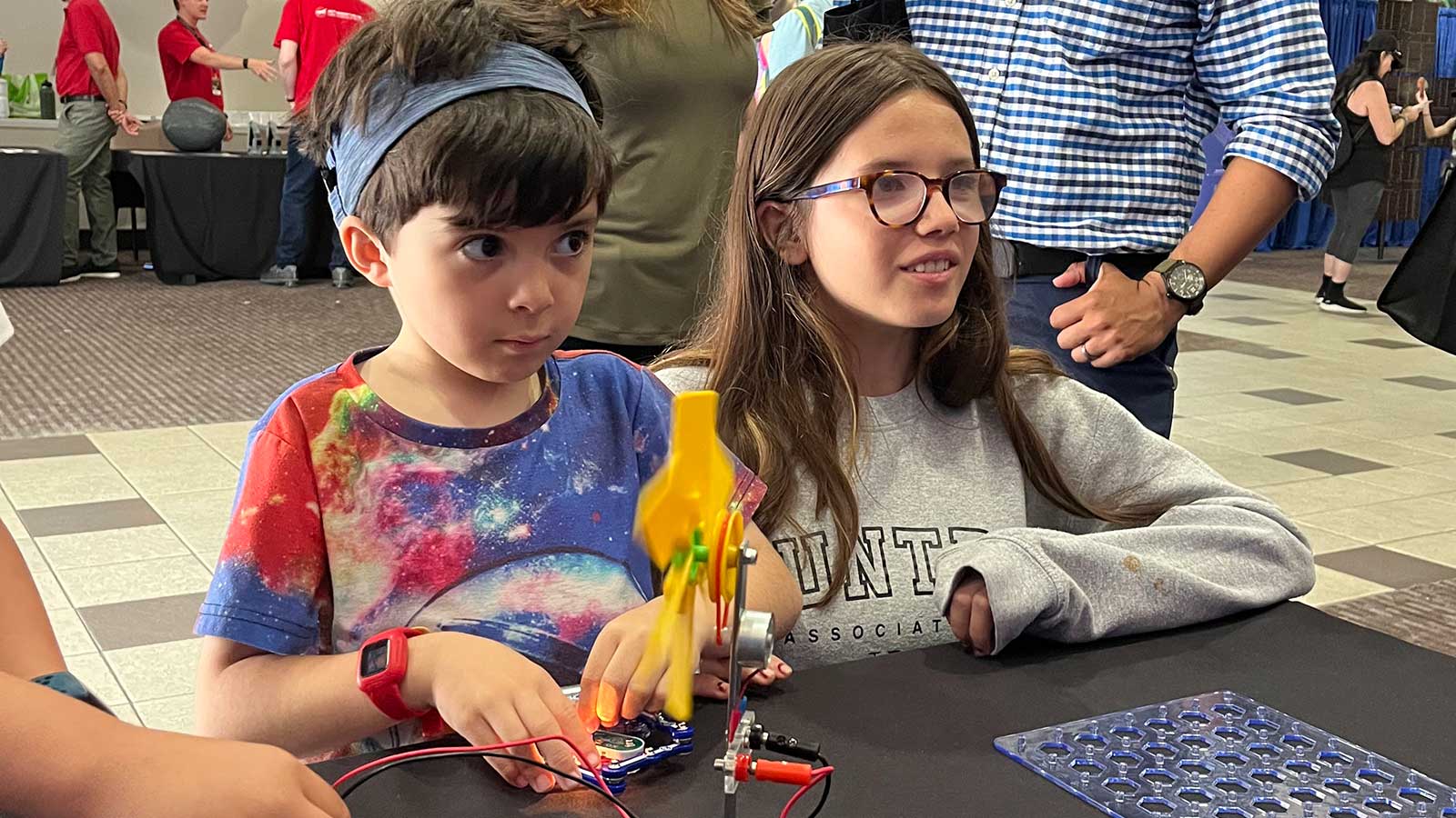 Two kids listen attentively to a scientist at a public event.