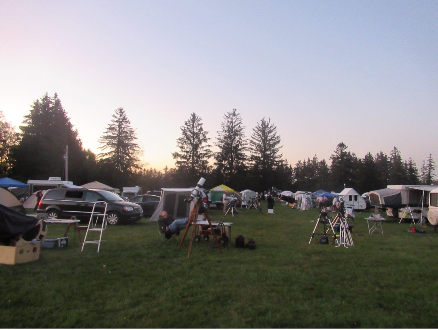 Tents, cars, and telescopes on a field beneath a blue and pink sky.