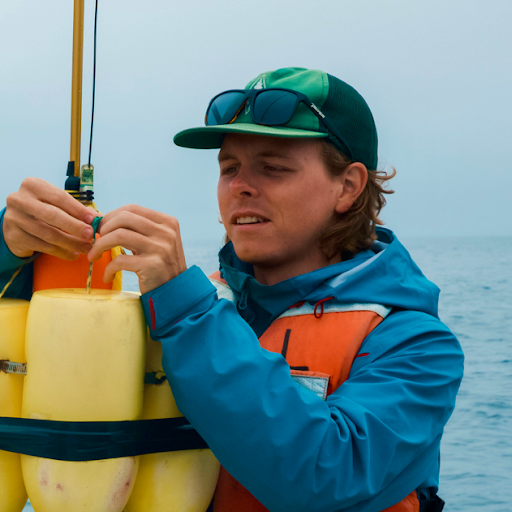 Photo of a man in a ball capand jacket tying equipment outside.