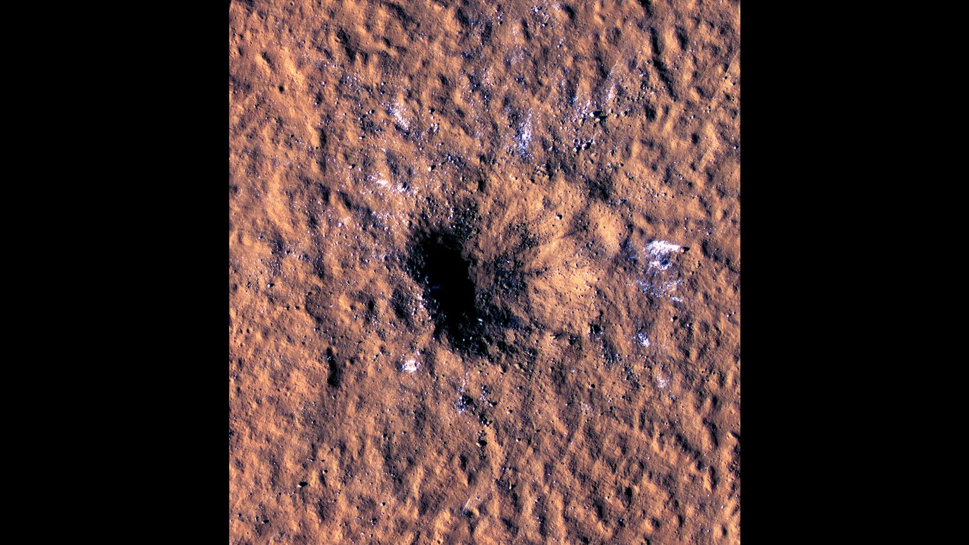 White chunks of ice stand out on the red sands of Mars surrounding this fresh impact crater.