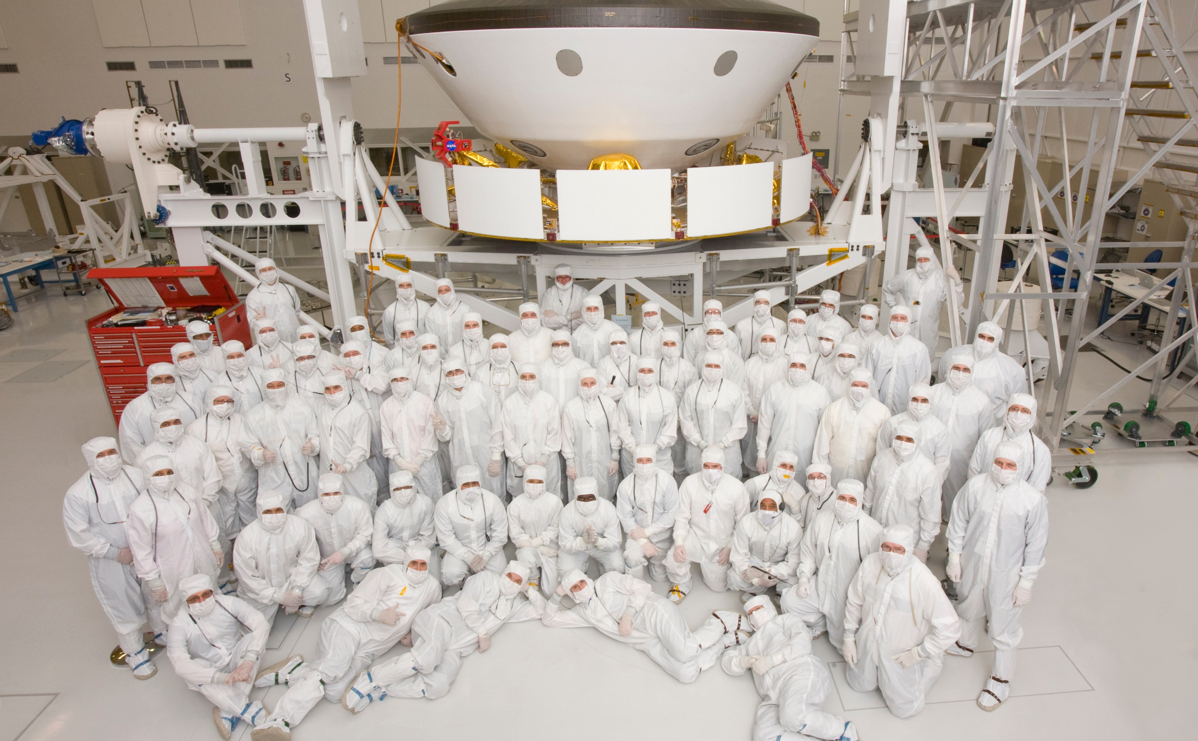 This photo shows 70 members of the Mars Science Laboratory team in Jet Propulsion Laboratory's Spacecraft Assembly Facility after they have prepared the spacecraft to go to a different area for the environmental tests.  The team members are dressed in "bunny suits" (white protective gear) and are positioned in various poses in front of the spacecraft.