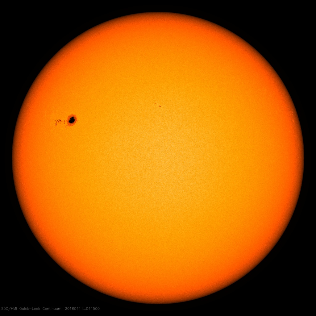 An image shows the Sun as an orange disk. In the upper left is a large sunspot with a few smaller sunspots to the left and right of it.