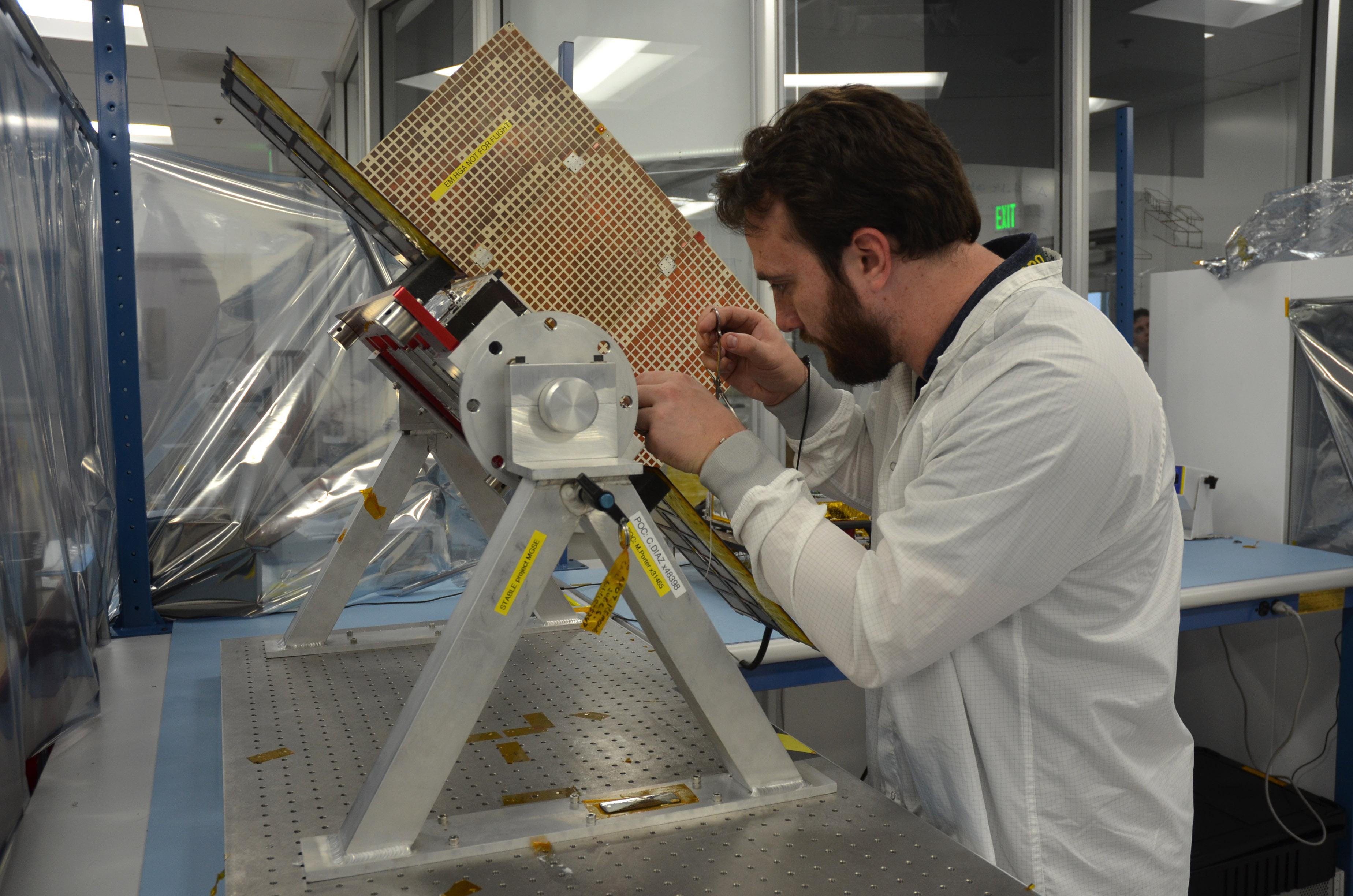 Joel Steinkraus, lead mechanical engineer for the MarCO (Mars Cube One) CubeSat spacecraft, adjusts a model of one of the two spacecraft.