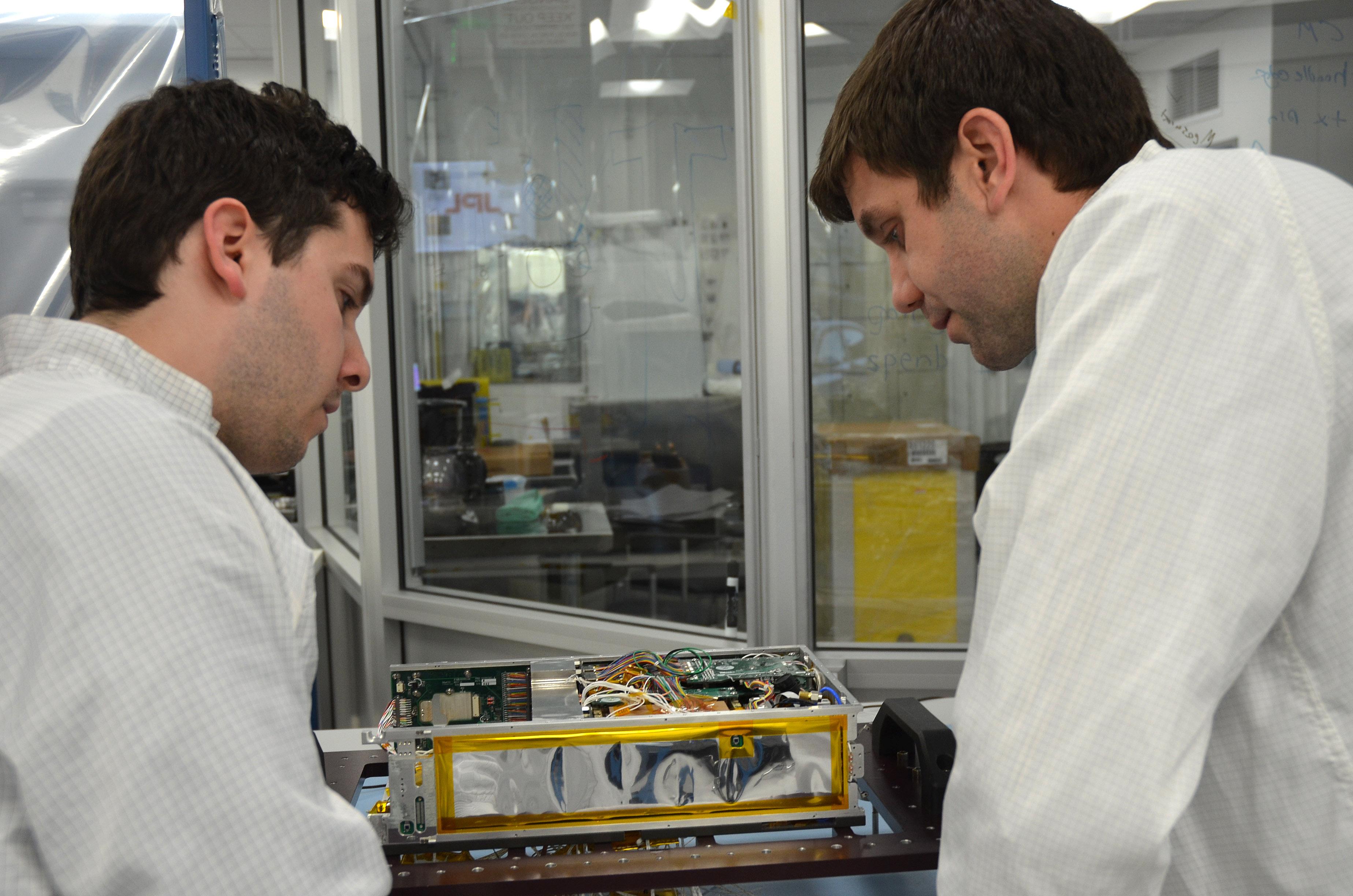 Engineers for NASA's MarCO (Mars Cube One) technology demonstration inspect one of the two MarCO CubeSats. Cody Colley, MarCO integration and test deputy, left, and Andy Klesh, MarCO chief engineer, are on the team at NASA's Jet Propulsion Laboratory, Pasadena, California, preparing twin MarCO CubeSats.