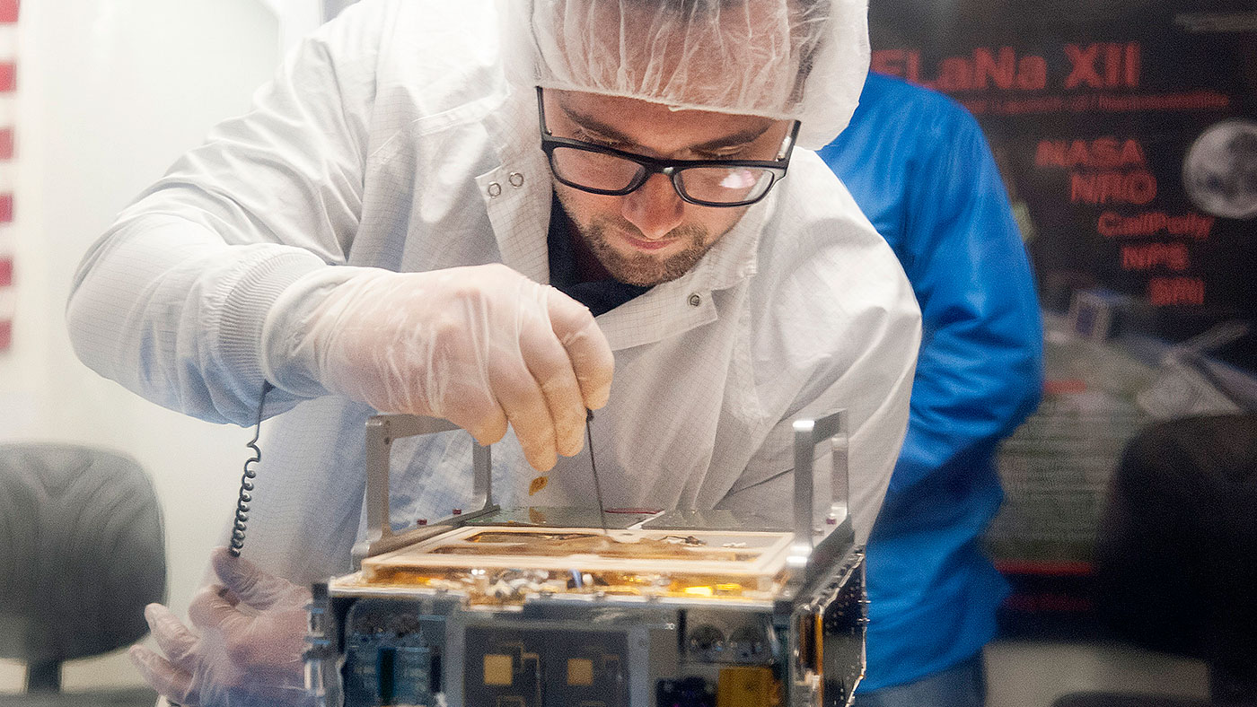 An engineer makes an adjustment on the CubeSat.