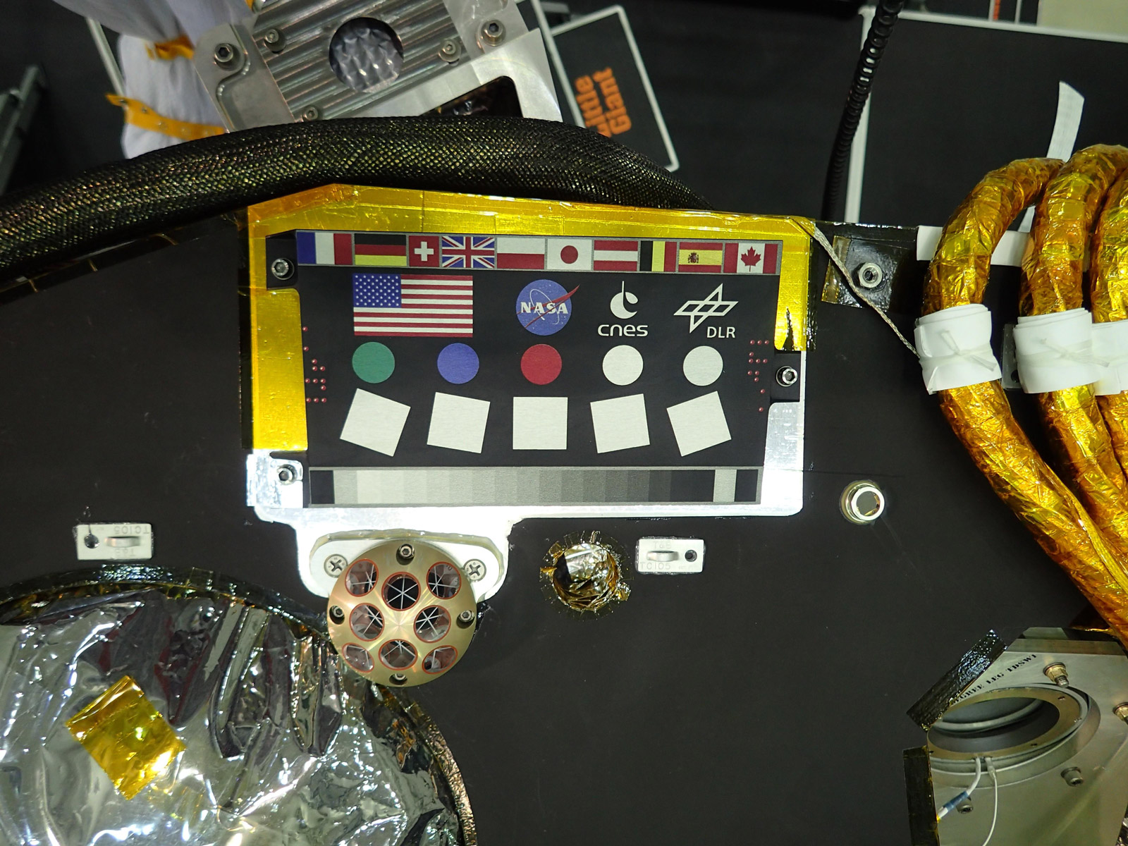 A camera calibration target sits on the deck of the NASA's InSight lander, adorned with the flags of the countries participating in the mission.