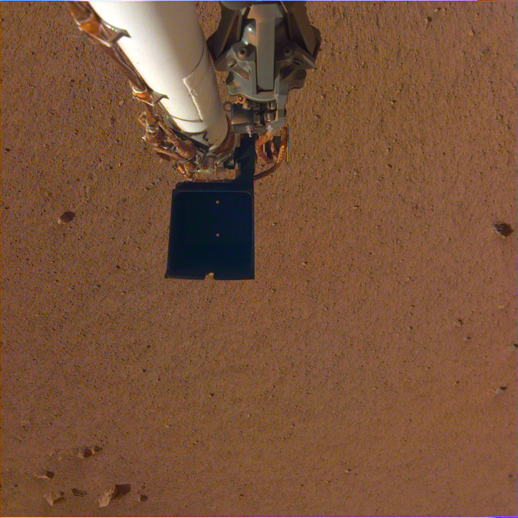 An image of InSight's robotic arm, with its scoop and stowed grapple, poised above the Martian soil. The image was received on Dec. 4, 2018 (Sol 8).