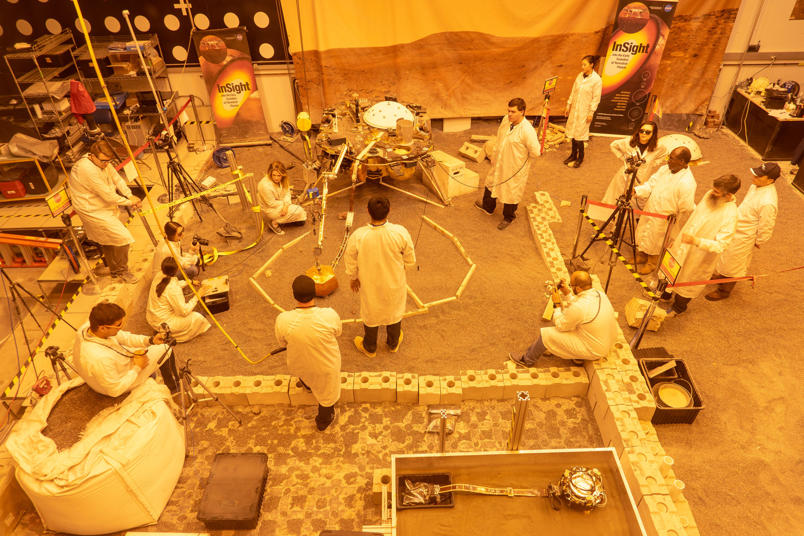 Engineers practice deploying InSight's instruments in a lab at NASA's Jet Propulsion Laboratory in Pasadena, California. Several of them are wearing sunglasses to block the bright yellow lights in the test space, which mimic sunlight as it appears on Mars.