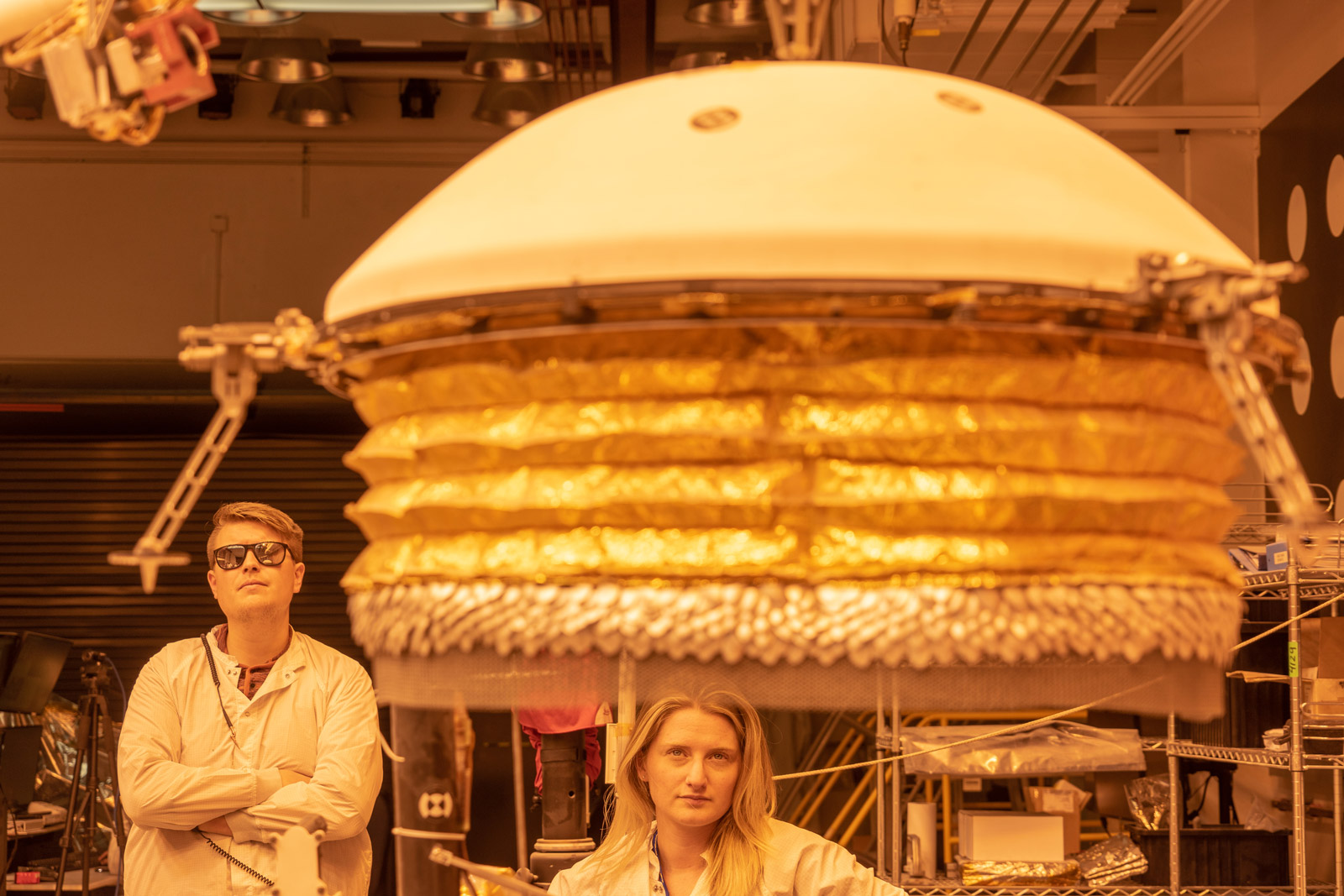 ForeSight, a fully functional, full-size model of NASA's InSight lander, practices deploying a model of the lander's Wind and Thermal Shield while engineers Phil Bailey (left) and Jaime Singer (center) look on. The Wind and Thermal Shield protects InSight's seismometer. This testing was done at NASA's Jet Propulsion Laboratory in Pasadena, California.