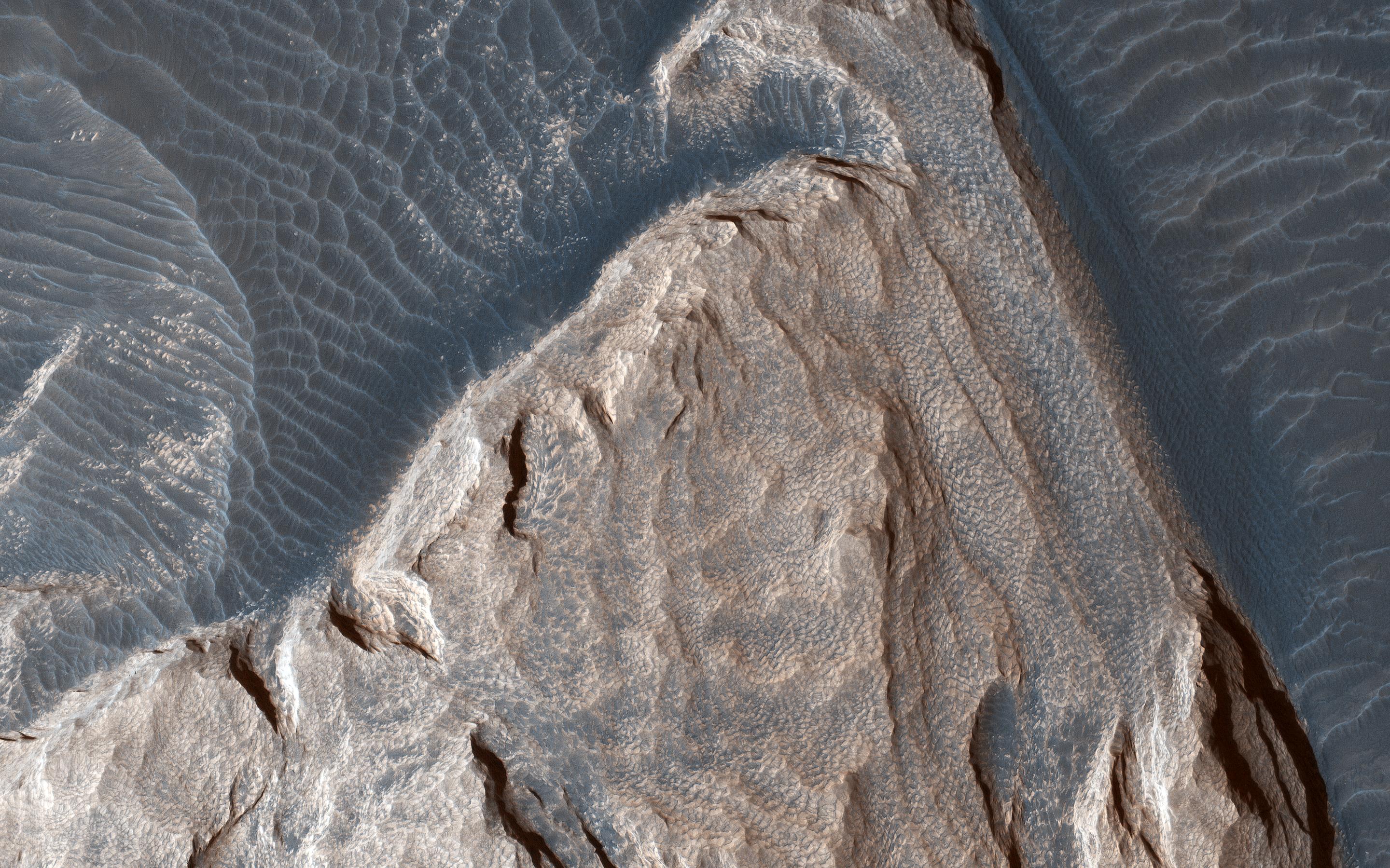 This image acquired on December 5, 2018 by NASAs Mars Reconnaissance Orbiter, shows ripples in the sand which tell us which way the wind was moving and how it was diverted around these rock formations.