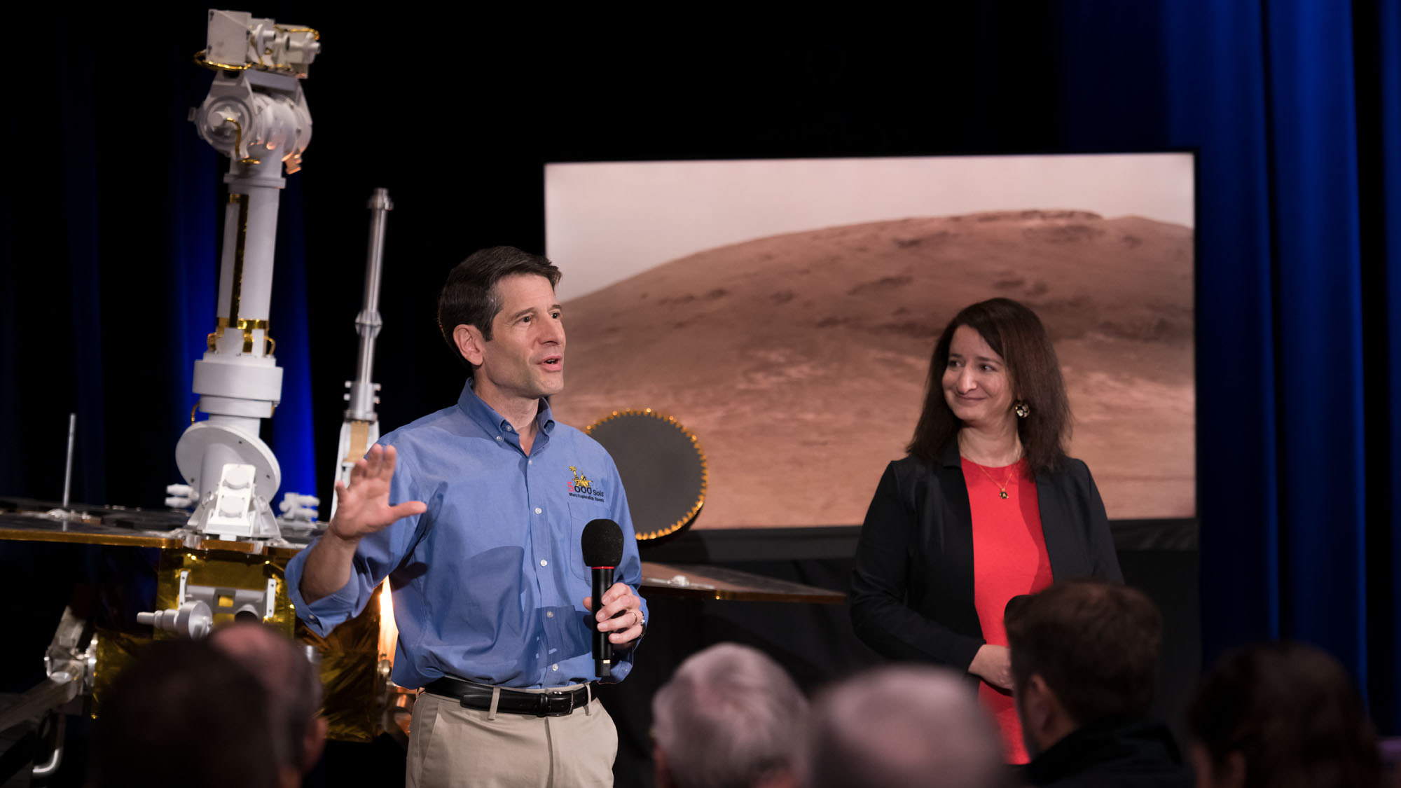With a model of NASA's Opportunity rover behind him, John Callas, project manager of the Spirit and Opportunity Mars rovers, speaks about the rovers' achievements at the agency's Jet Propulsion Laboratory in Pasadena, California. Deputy Project Scientist Abigail Fraeman (right) looks on.