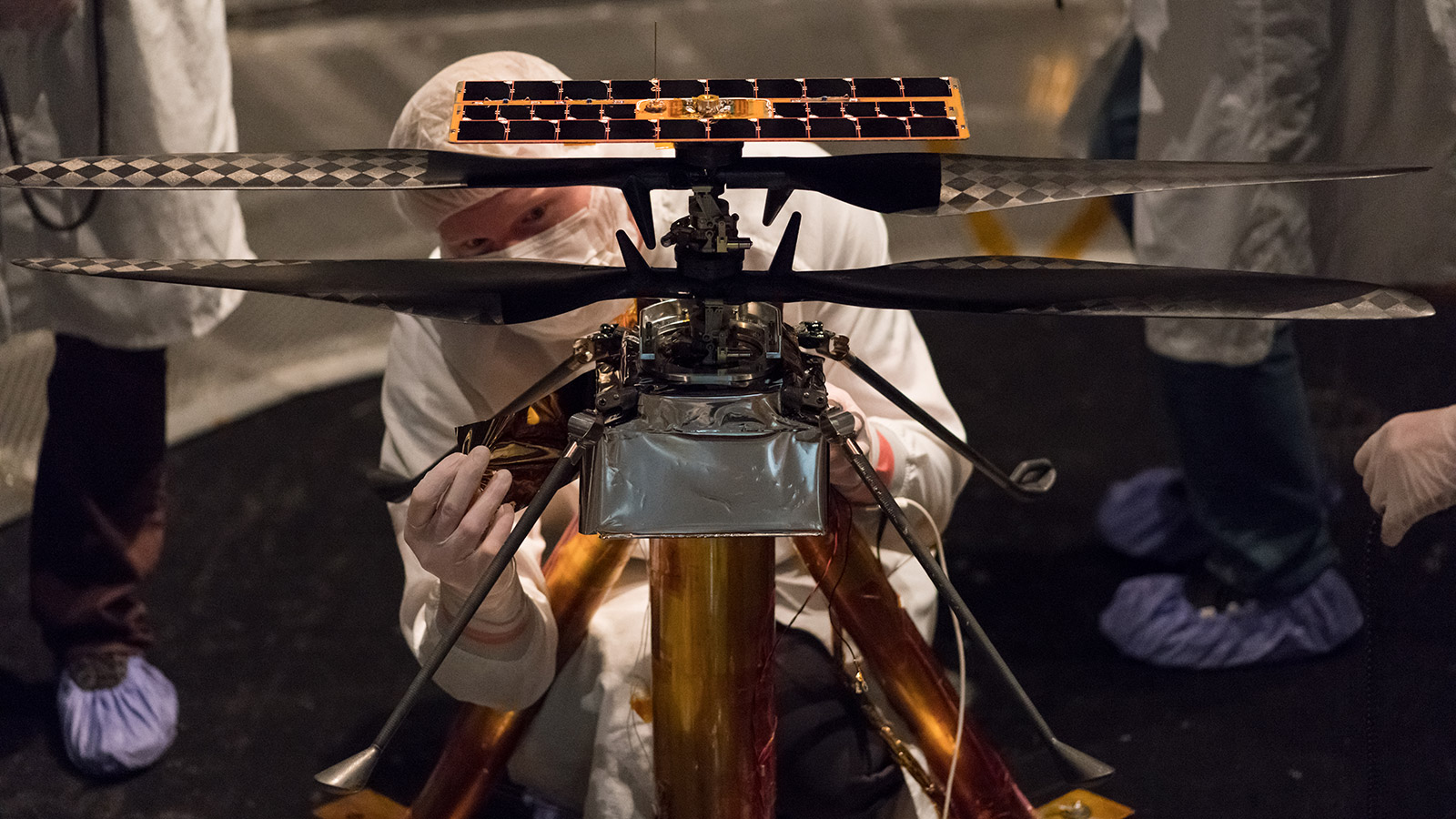 Members of the NASA Mars Helicopter team attach a thermal film to the exterior of the flight model of the Mars Helicopter.