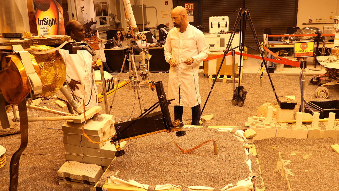 Engineers in a Mars-like test area at NASA's Jet Propulsion Laboratory try possible strategies to aid the Heat Flow and Physical Properties Package (HP3) on NASA's InSight lander, using engineering models of the lander, robotic arm and instrument.