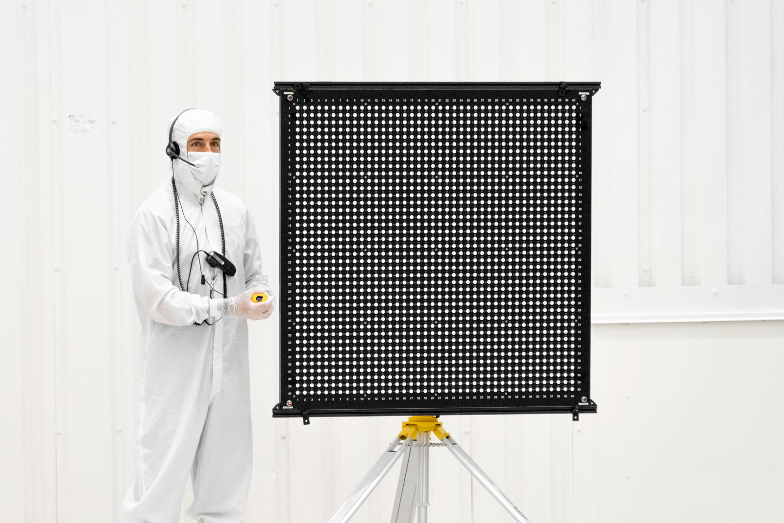 Engineer Chris Chatellier stands next to a target board with 1,600 dots. The board was one of several used on July 23, 2019, in the Spacecraft Assembly Facility's High Bay 1 at NASA's Jet Propulsion Laboratory in Pasadena, California, to calibrate the forward-facing cameras on the Mars 2020 rover.
