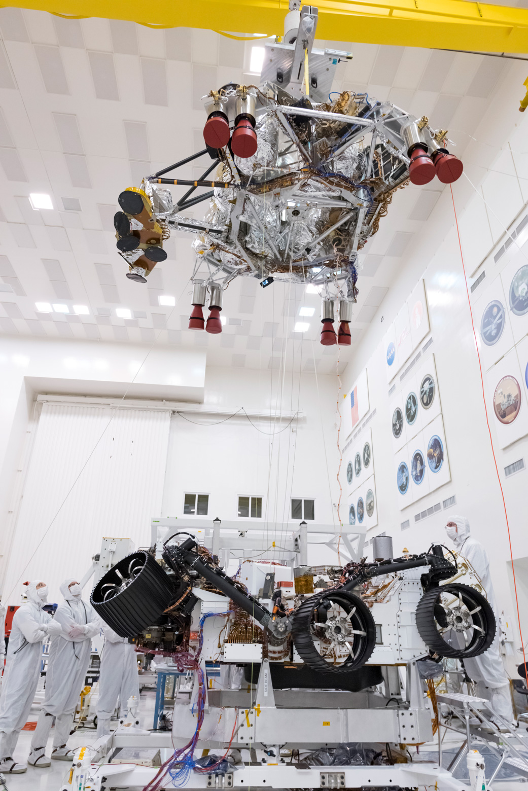 Engineers and technicians working on the Mars 2020 spacecraft look on as a crane lifts the rocket-powered descent stage away from the rover after a test.
