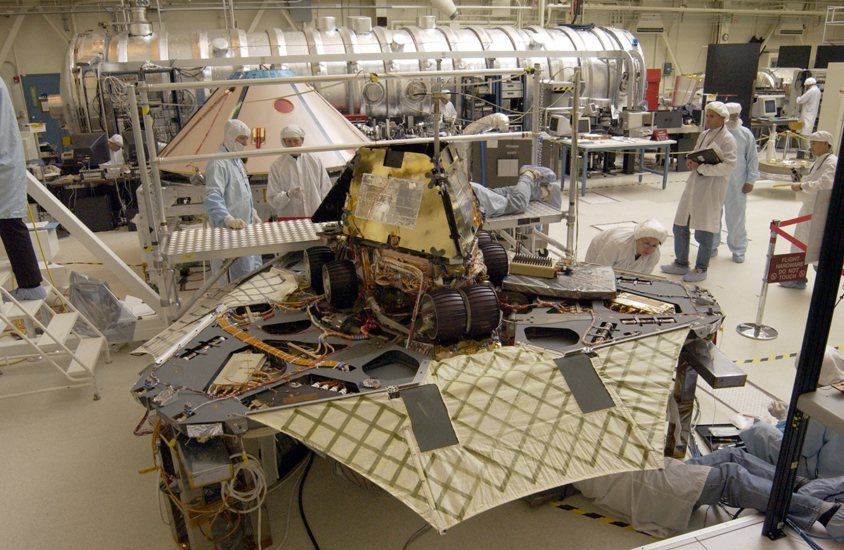 A "Martian mechanic" checks beneath the completely deployed Rover 1 lander. Atop the lander is Rover 1 with its wheels and solar arrays in the stowed position.