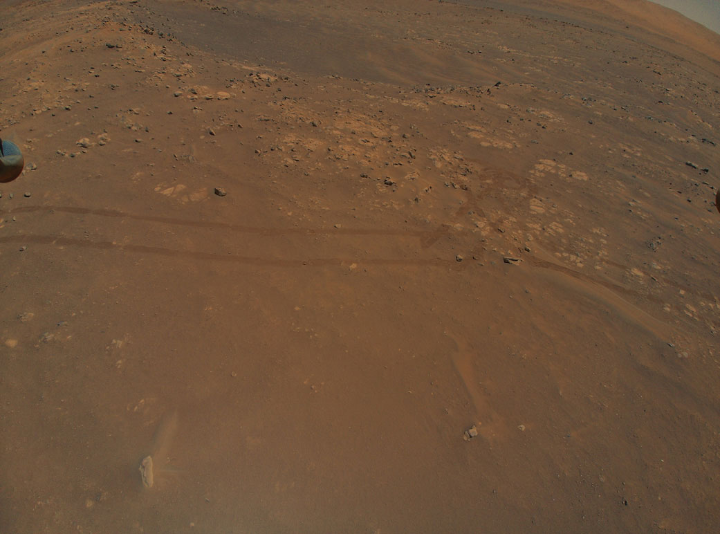 This is a colored image of the sandy surface of Mars. There are small rocks and marks of the rovers wheels on the sandy surface.