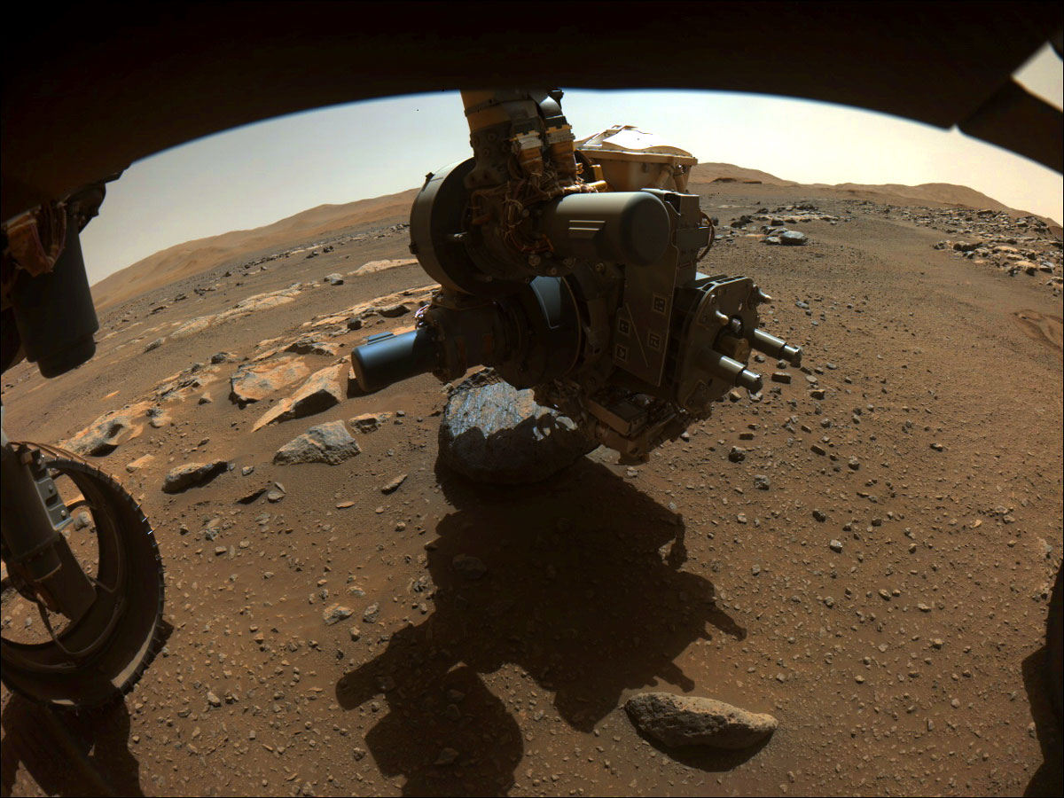 This is a colored image of the Perseverance rover capturing the science-instrument-laden turret at the end of its robotic arm getting close to the rock nicknamed "Rochette." The sandy surface of Mars and hills can be seen in the background of this image.