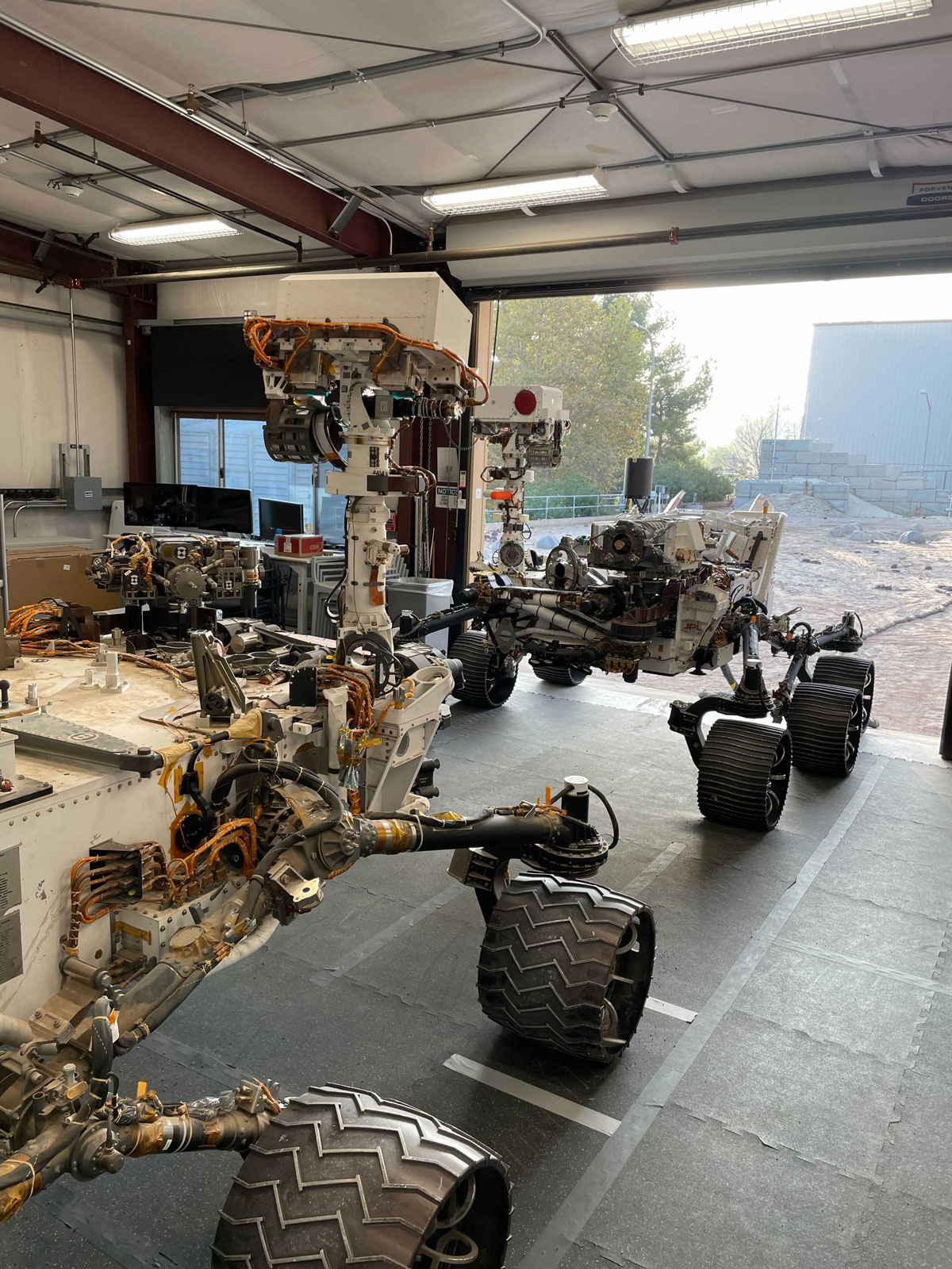 Engineering models of the Curiosity Mars rover (foreground) and the Perseverance Mars rover share space in the garage at JPL’s Mars Yard.