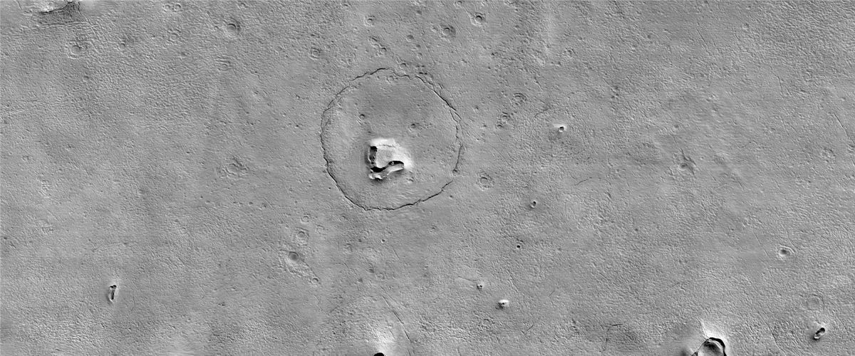 This image taken in December 2022 by HiRISE on MRO appears to show a bear's face on the Mars' surface, made up of a hill, craters and a circular fracture pattern.