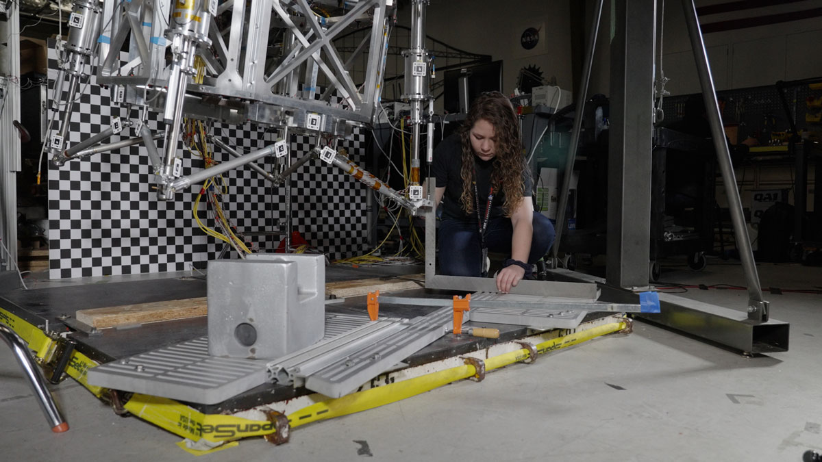 Morgan Montalvo, another JPL engineer, sets guardrails on the floor below the prototype in a test of a scenario where the lander would “stub a toe” against a rock while touching down on Mars.