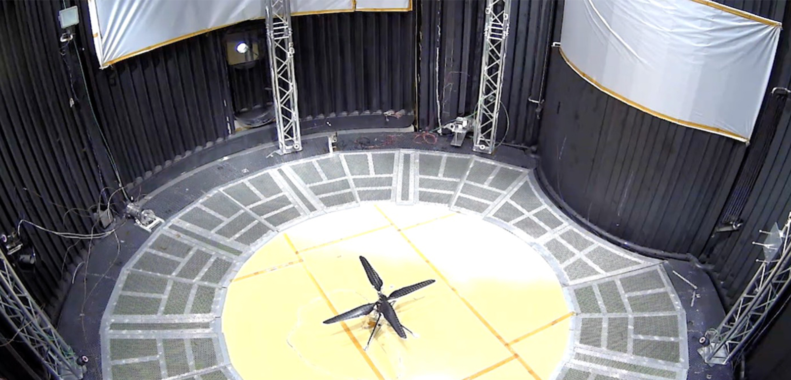 This image shows a test flight of a full-scale prototype of the Ingenuity Mars Helicopter within a chamber at the Space Simulator Facility at Jet Propulsion Laboratory.