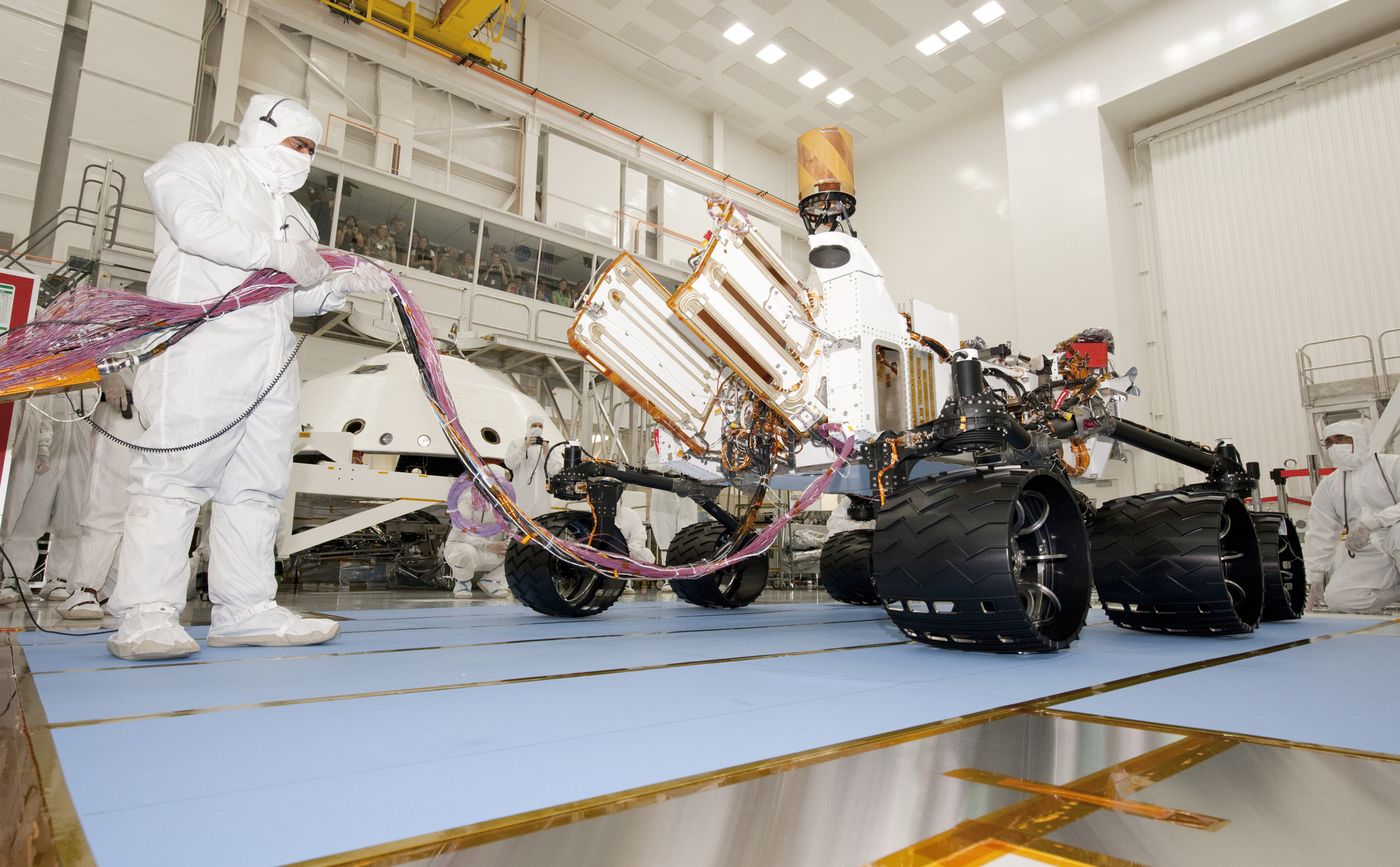 A test operator in clean-room garb holds umbilical cables for NASA's Mars rover Curiosity during the rover's first drive test, on July 23, 2010.