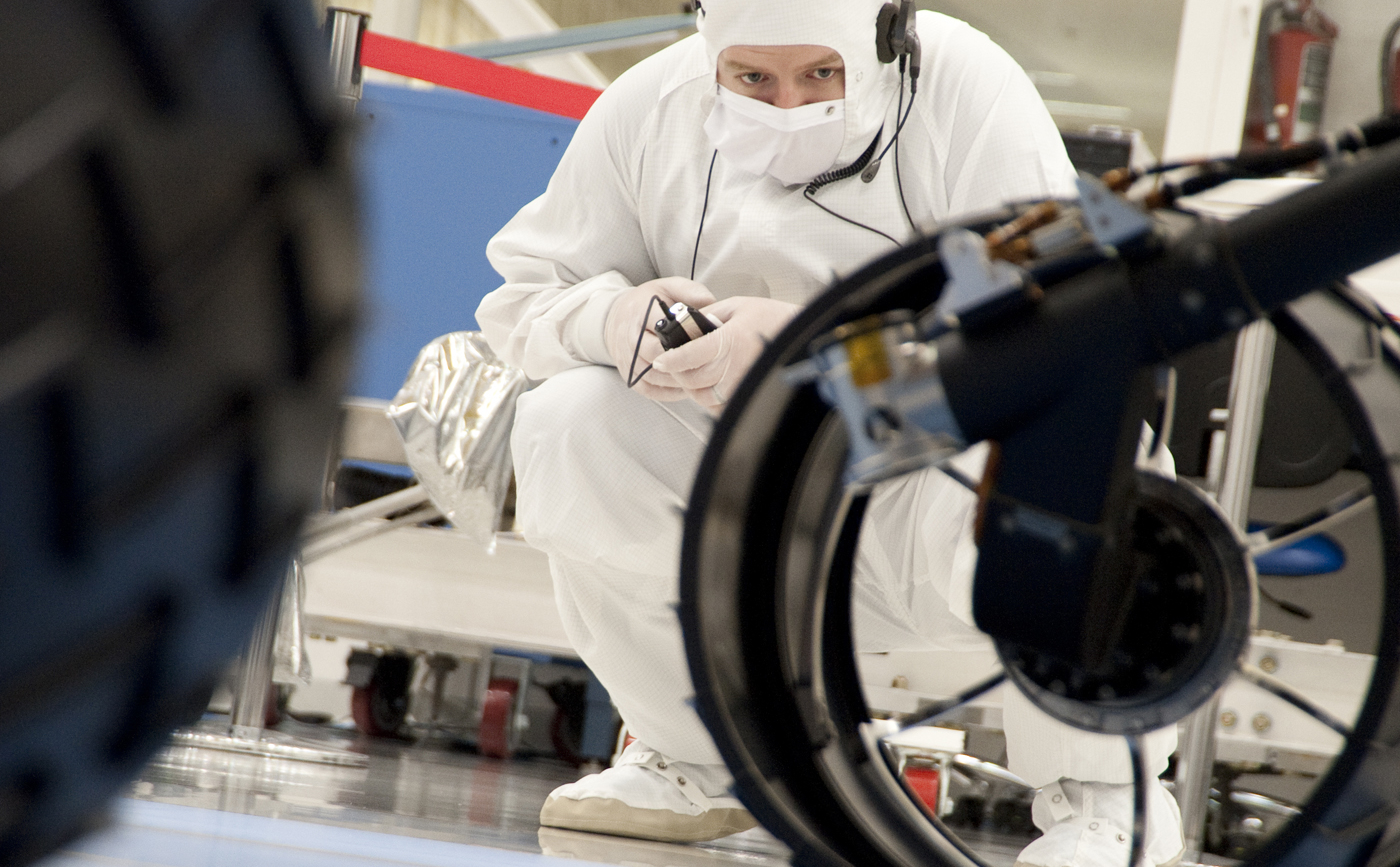 A test operator in clean-room garb observes rolling of the wheels during the first drive test of NASA's Curiosity rover, on July 23, 2010.