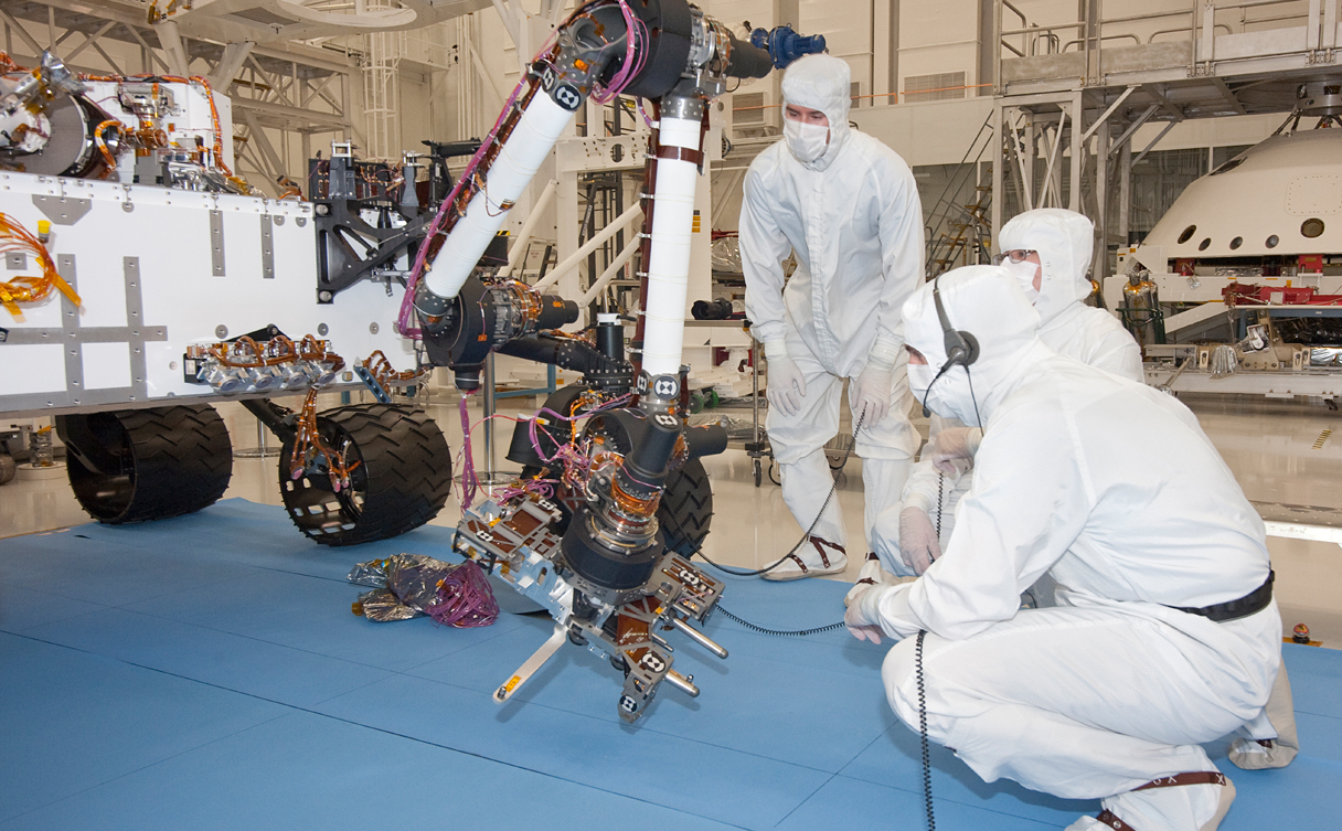 Test operators in a clean room at NASA's Jet Propulsion Laboratory, Pasadena, Calif., monitor some of the first motions by the robotic arm on the Mars rover Curiosity after installation in August 2010. This photo, taken Aug. 31, 2010, shows the arm in a partially extended position. The arm has a reach of about 2.3 meters (7.5 feet) from the front of the rover body.