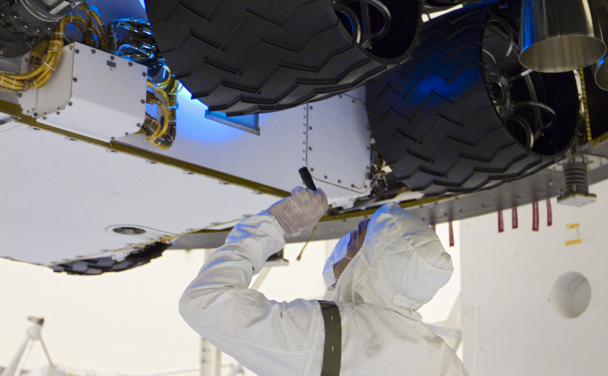 In the Payload Hazardous Servicing Facility at NASA's Kennedy Space Center in Florida, a technician inspects beneath NASA's Mars Science Laboratory (MSL) mission aeroshell, (containing the compact car-sized rover Curiosity), which has been mated to the cruise stage.