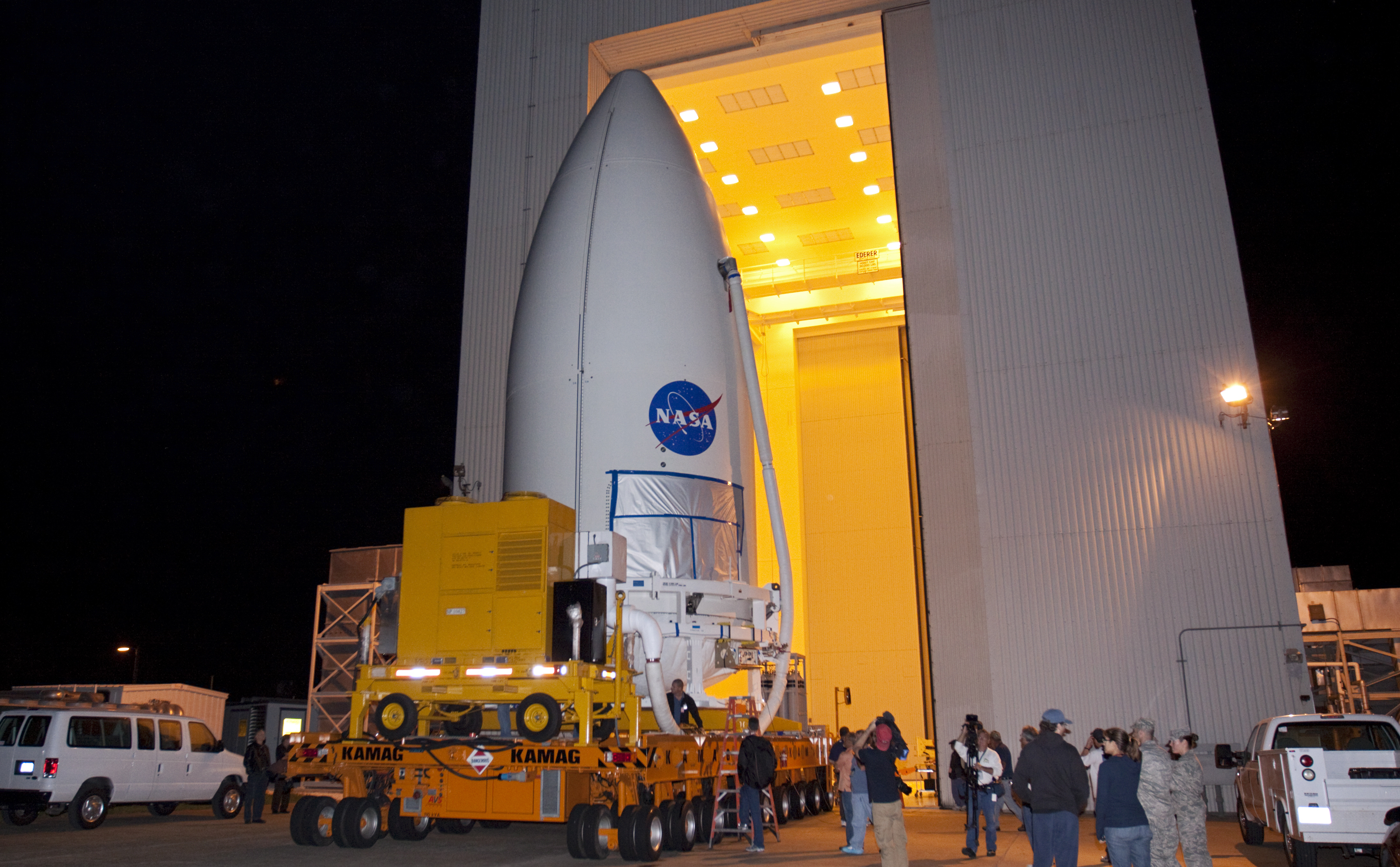 Standing atop a payload transporter, the Atlas V rocket payload fairing containing NASA's Mars Science Laboratory (MSL) spacecraft rolls out of the Payload Hazardous Servicing Facility at Kennedy Space Center in Florida, beginning the move to Space Launch Complex 41.