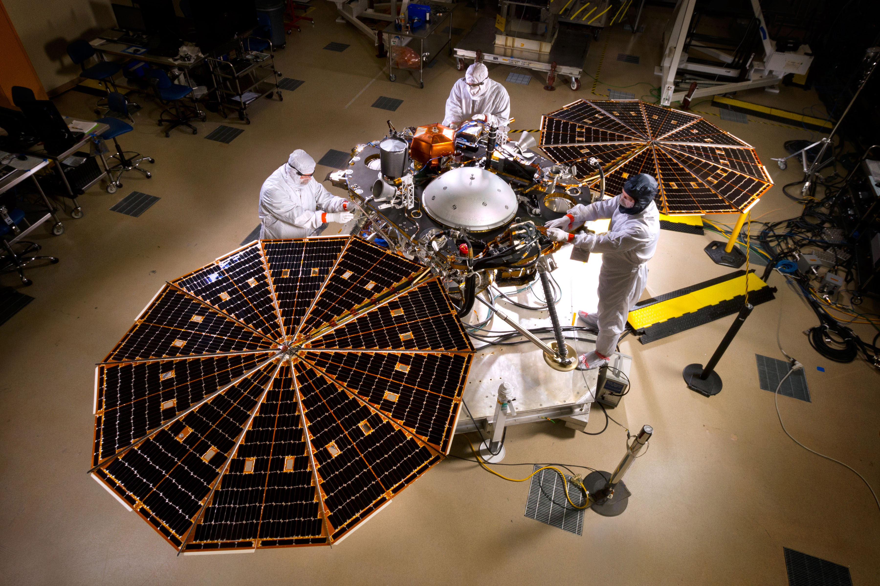 The insight lander is fully opened with solar panels spread wide for this cleanroom photo. Several engineers are working on the rover.