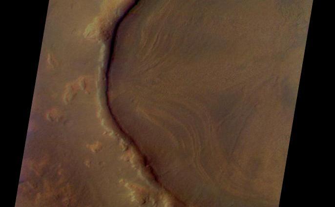 This is a Mars Odyssey visible color image of an unnamed crater in western Arcadia Planitia (near 39 degrees N, 179 degrees E). The crater shows a number of interesting internal and external features that suggest that it has undergone substantial modification since it formed. These features include concentric layers and radial streaks of brighter, redder materials inside the crater, and a heavily degraded rim and ejecta blanket. The patterns inside the crater suggest that material has flowed or slumped towards the center. Other craters with features like this have been seen at both northern and southern mid latitudes The distribution of these kinds of craters suggests the possible influence of surface or subsurface ice in the formation of these enigmatic features. The image was taken on September 29, 2002 during late northern spring. This is an approximate true color image, generated from a long strip of visible red (654 nm), green (540 nm), and blue (425 nm) filter images that were calibrated using a combination of pre-flight measurements and Hubble images of Mars. The colors appear perhaps a bit darker than one might expect; this is most likely because the images were acquired in late afternoon (roughly 4:40 p.m. local solar time) and the low Sun angle results in an overall darker surface.