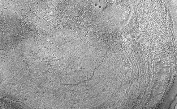 This Mars Global Surveyor (MGS) Mars Orbiter Camera (MOC) image shows the interior of a typical crater in northern Acidalia Planitia. The floor is covered by material that forms an almost concentric pattern. In this case, the semi-concentric rings might be an expression of eroded layered material, although this interpretation is uncertain. The crater is located near 44.0°N, 27.7°W, and covers an area about 3 km (1.9 mi) wide. Sunlight illuminates the scene from the lower left.
