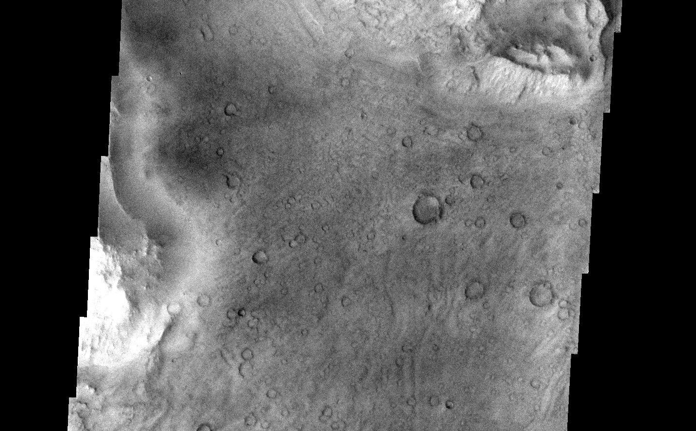 This image is located near the boundary between Syrtis Major and Isidis Planitia. The top of the image shows rough material that has eroded away from the lower portion of the image, revealing an underlying surface that has many small craters. It also reveals an ancient flow lobe that is barely discernable, crossing the southern part of the image (this flow lobe is much easier to see as a smooth region in the context image).