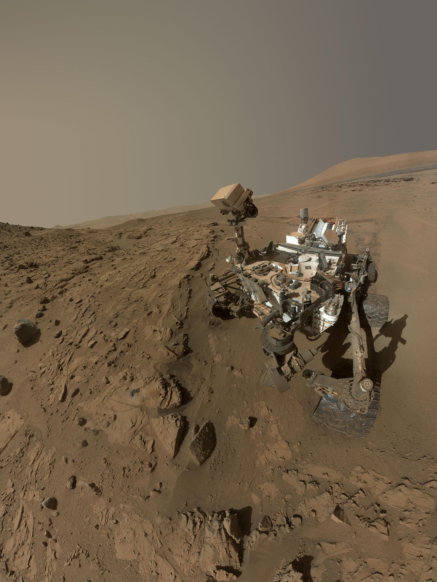 Curiosity, rover, self-portrait, rock, drilling, windjana, waypoint, kimberley - This image is a self-portrait of the Curiosity rover taken from the site with the rover's 'head' down, with rock formations surrounding it and Mount Sharp in the background.
