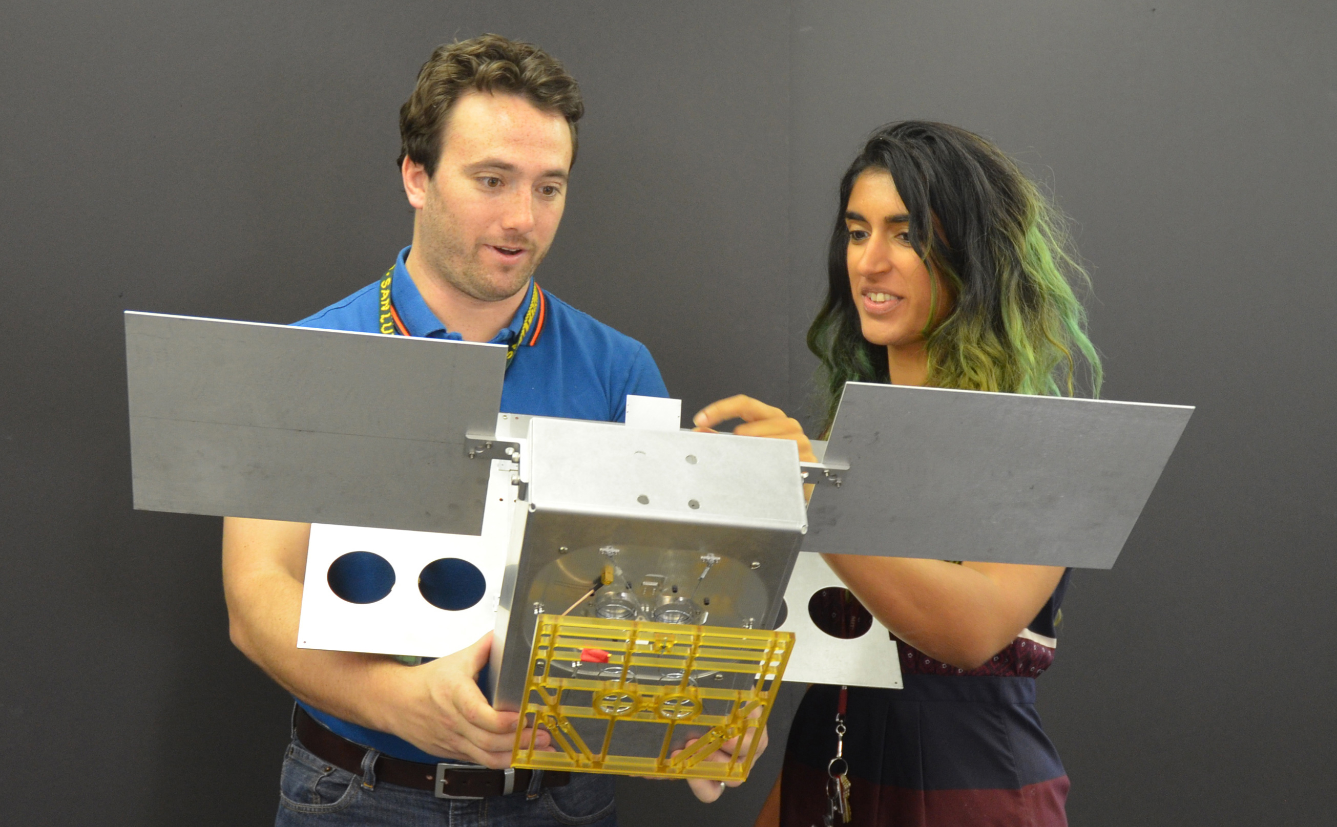 Two engineers hold a full-scale mechanical mock-up of a small satellite.