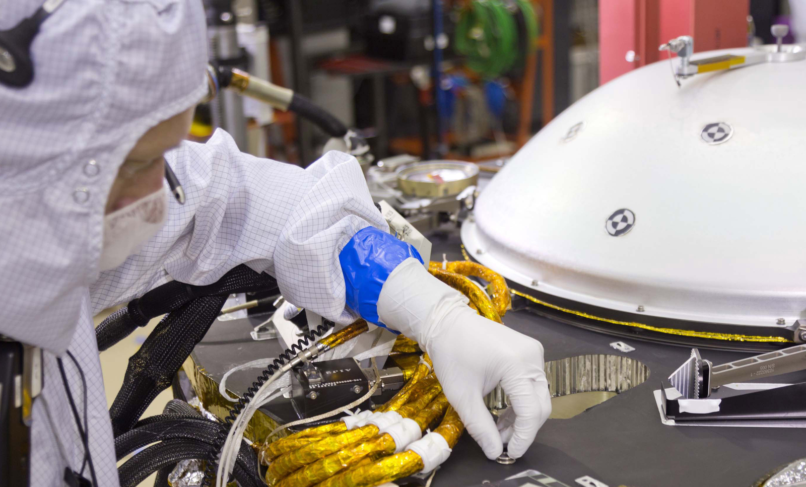 A spacecraft specialist in a clean room at Lockheed Martin Space Systems in Denver, where the InSight lander is being built, affixes a dime-size chip onto the lander deck in November 2015.