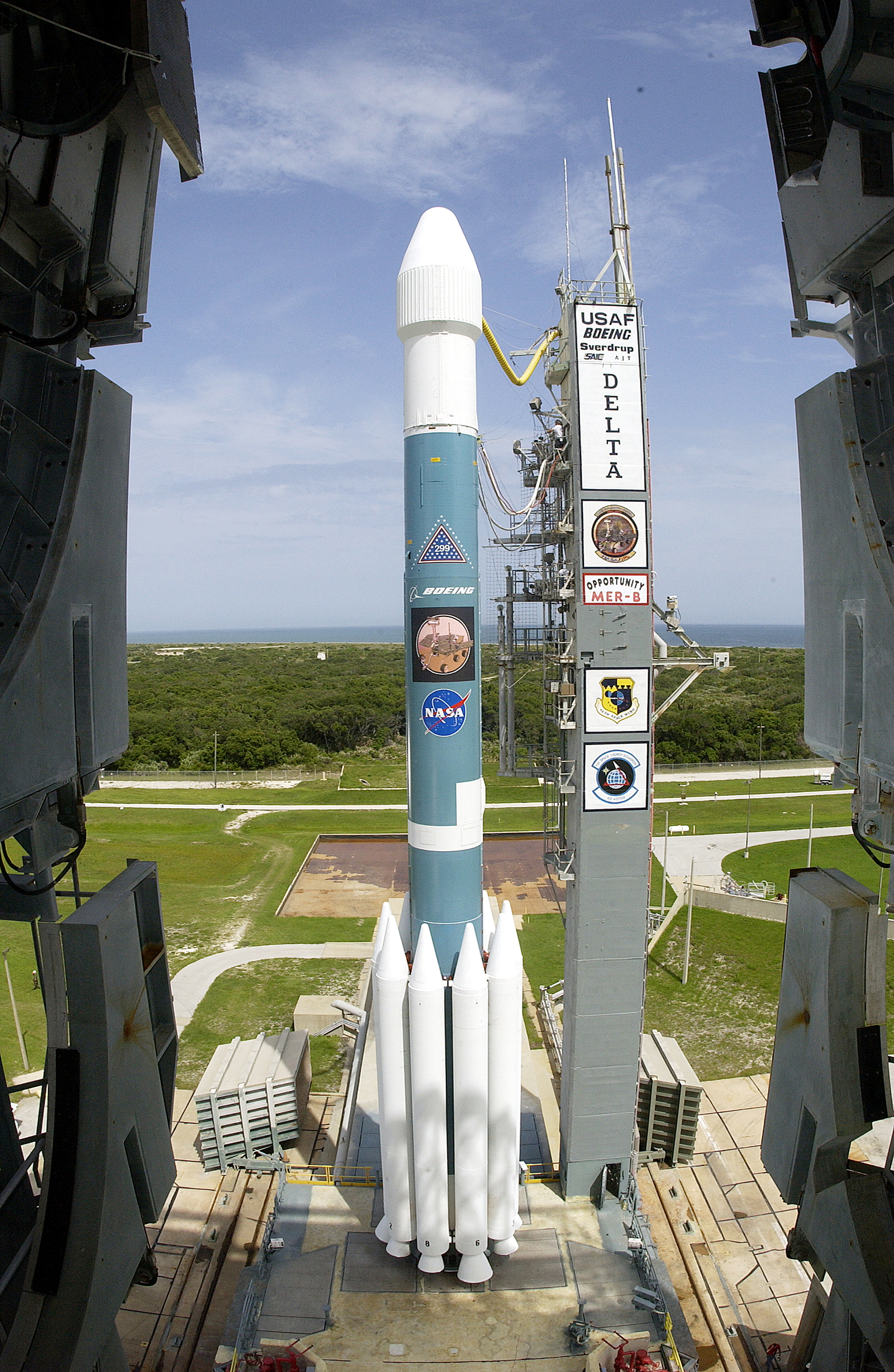 A large blue and white rocket that houses the Opportunity rover sits on a launch pad at Cape Canaveral, Florida.  Nine solid rocket boosters that provide an extra push circle the first stage of the rocket.