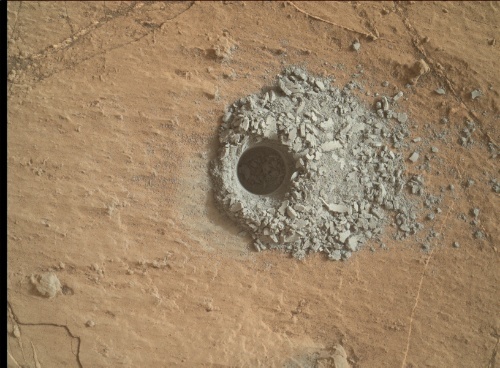 Studying drill "tailings," gray material surrounding the drill hole.